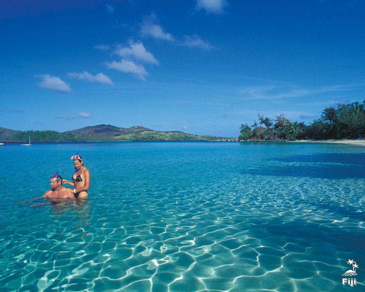 Fiji 桌布 壁紙 — 一對情侶穿著浮潛裝備漂浮在清澈碧綠的海水中，天空蔚藍，白雲點點。