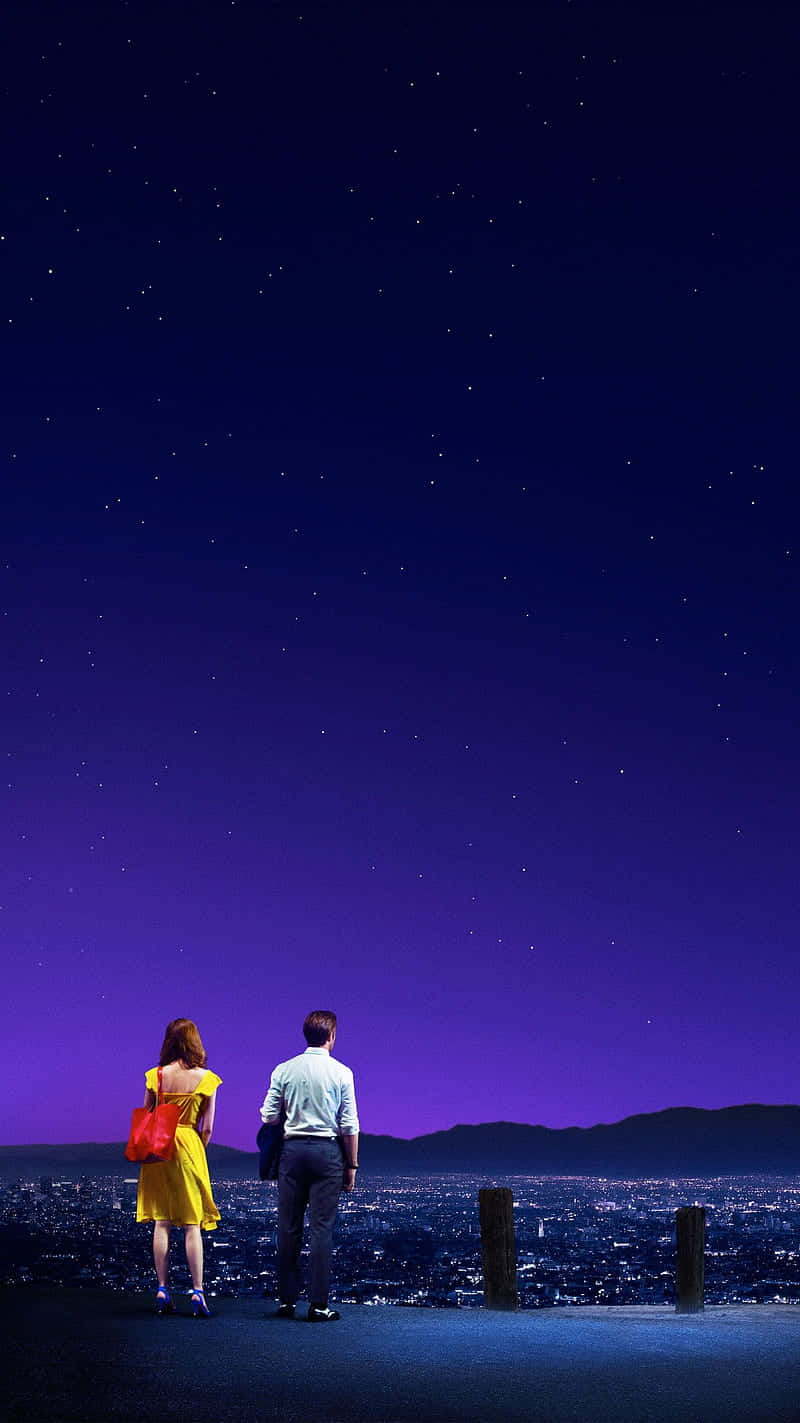 La La Land 4K 桌布 壁紙 — 一對情侶站在山丘上，俯瞰著廣闊星空下閃耀的城市。