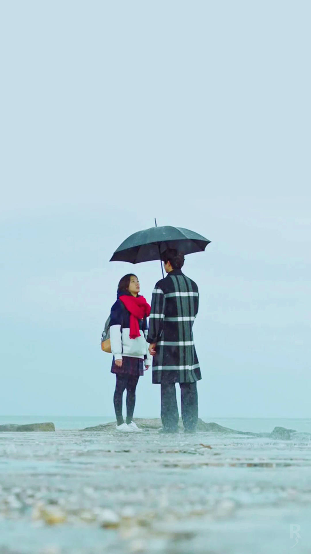 drama 桌布 壁紙 — 一對情侶站在霧濛濛的海灘上，撐著黑色雨傘，手牽手，周圍下著雨。