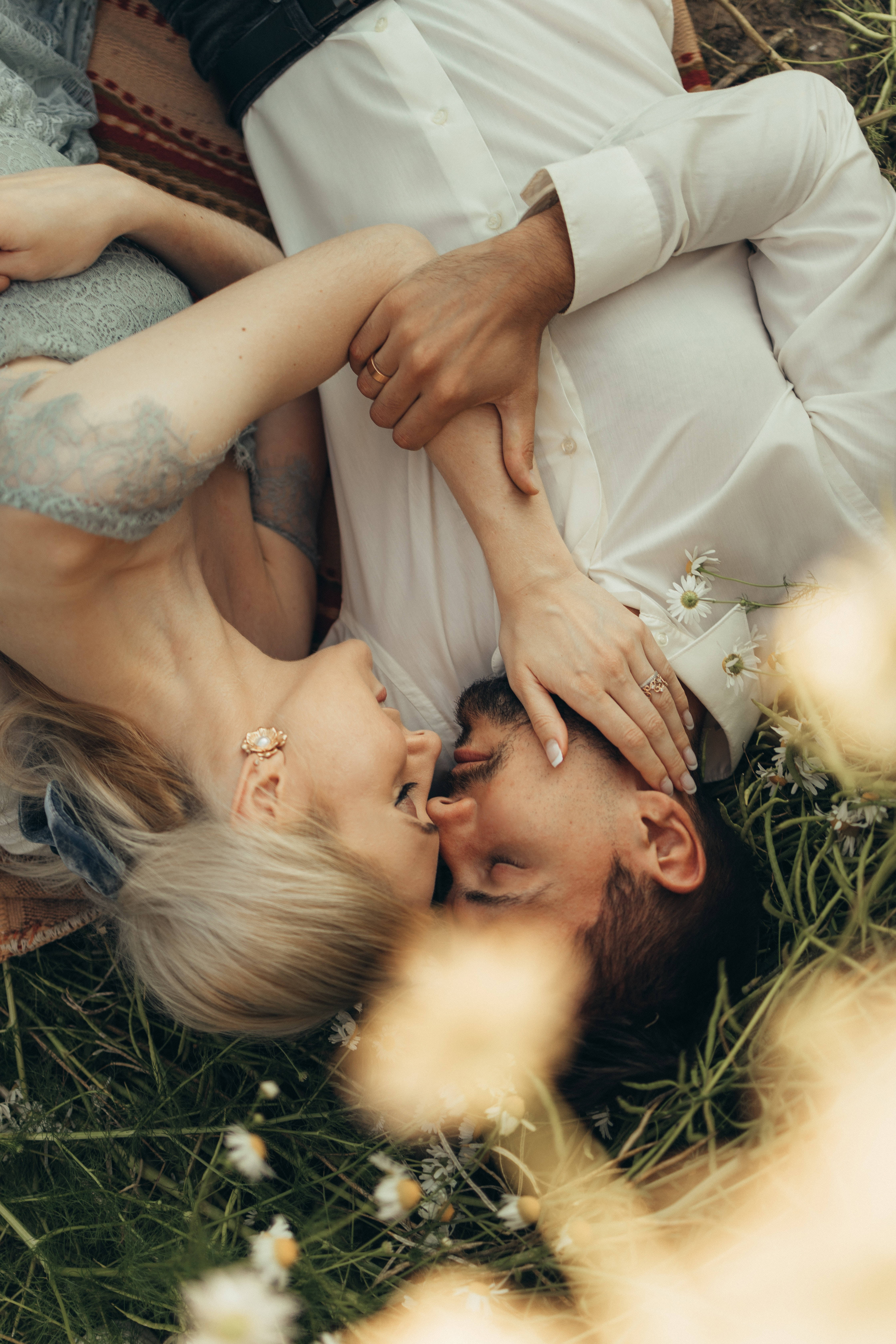 caressing 桌布 壁紙 — 一對情侶纏綿地躺在草地上，在雛菊和柔和陽光的環繞下深情對望。