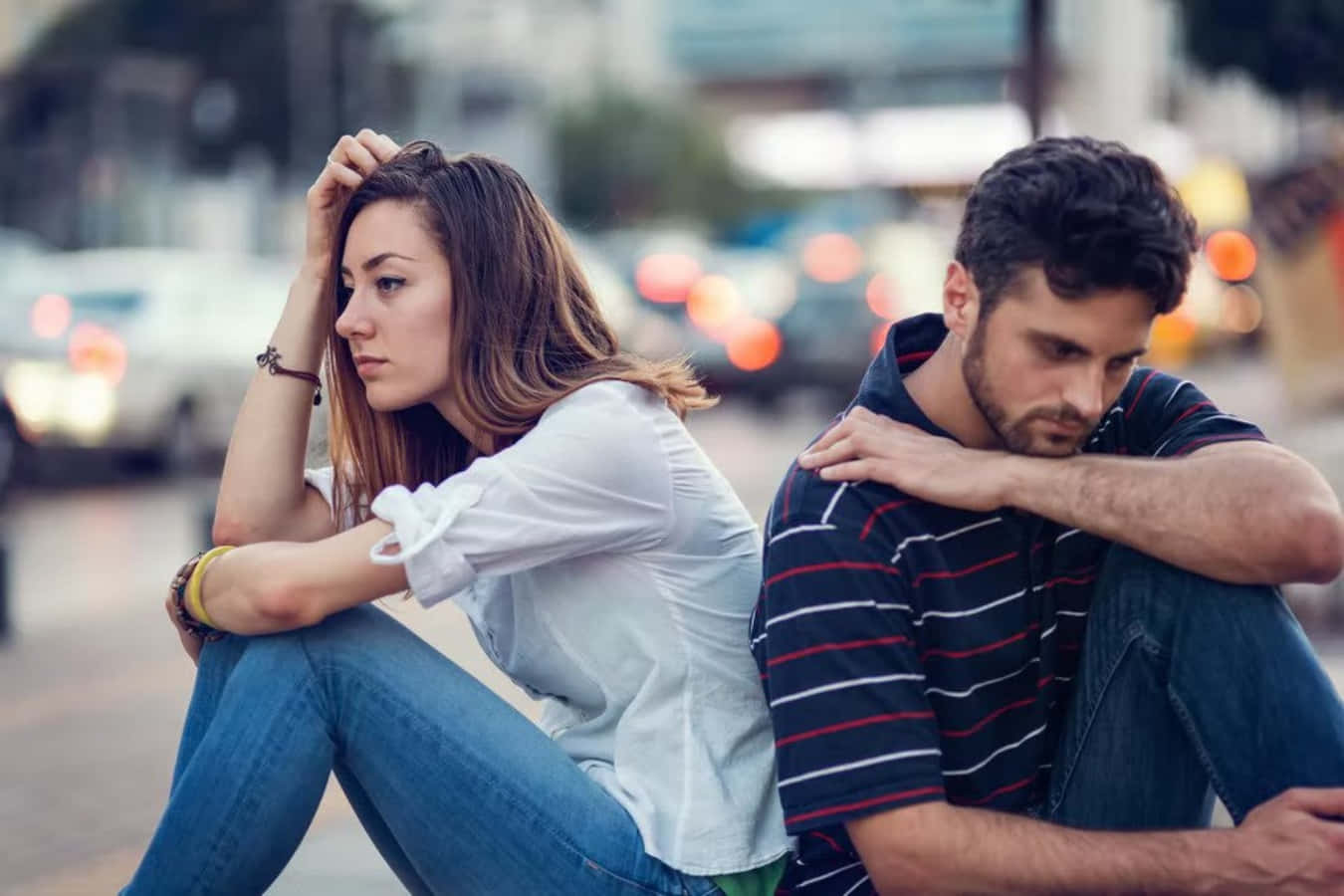 Breakup Couple 桌布 壁紙 — 一對情侶背對背坐在城市人行道上，看起來很傷心，身後有模糊的車燈掠過。