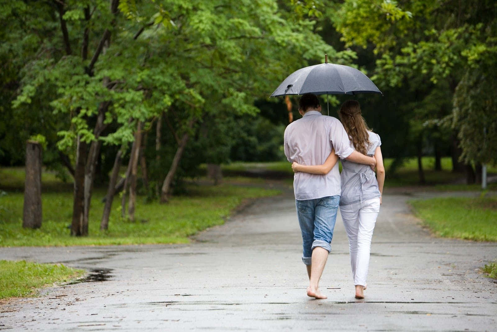 Umbrella 桌布 壁紙 — 一對情侶赤腳撐傘走在潮濕的公園小徑上，四周綠樹成蔭。