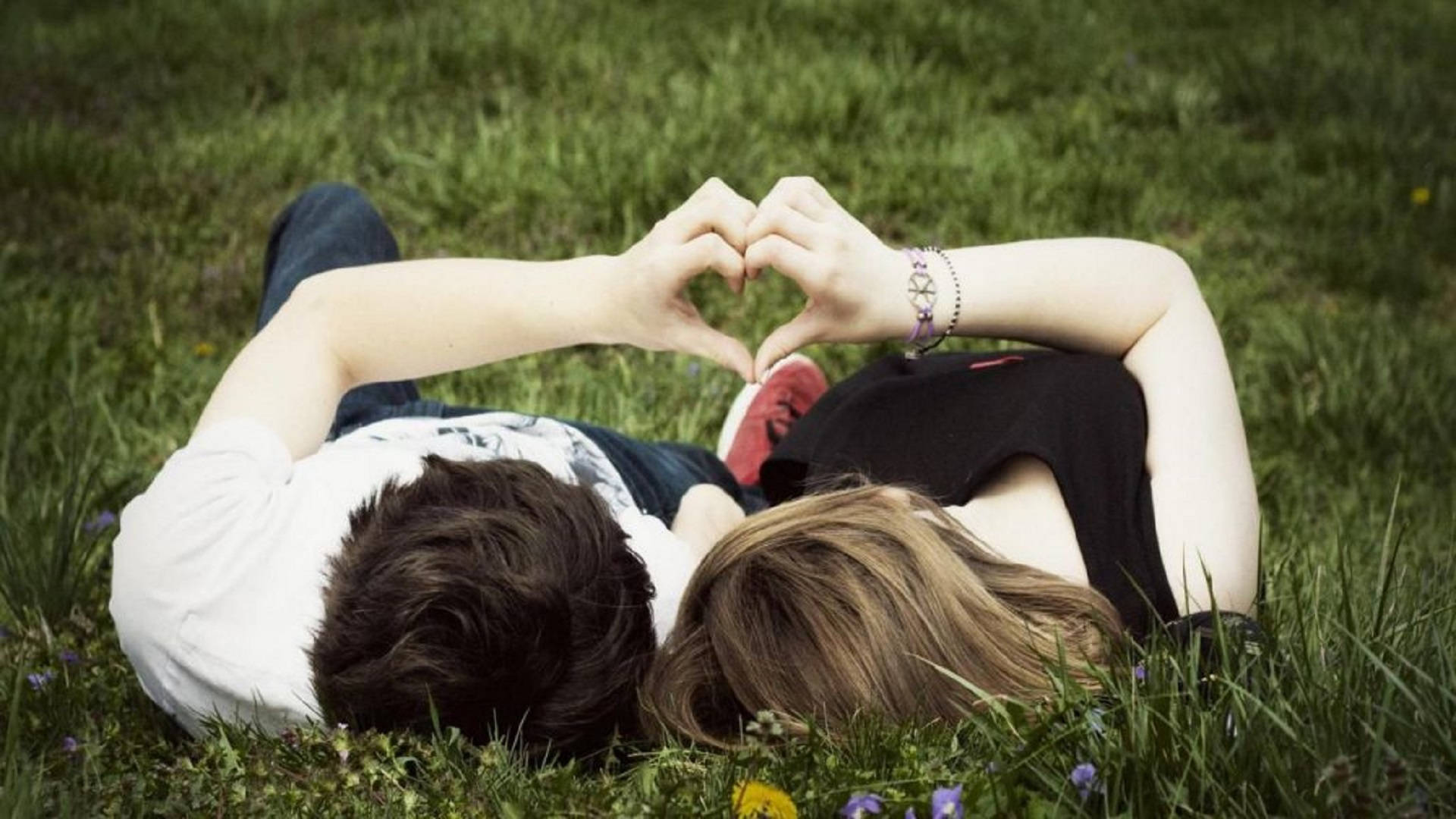 Romantic Love 桌布 壁紙 — 一對情侶躺在草地上，被野花環繞，用手比出心形。