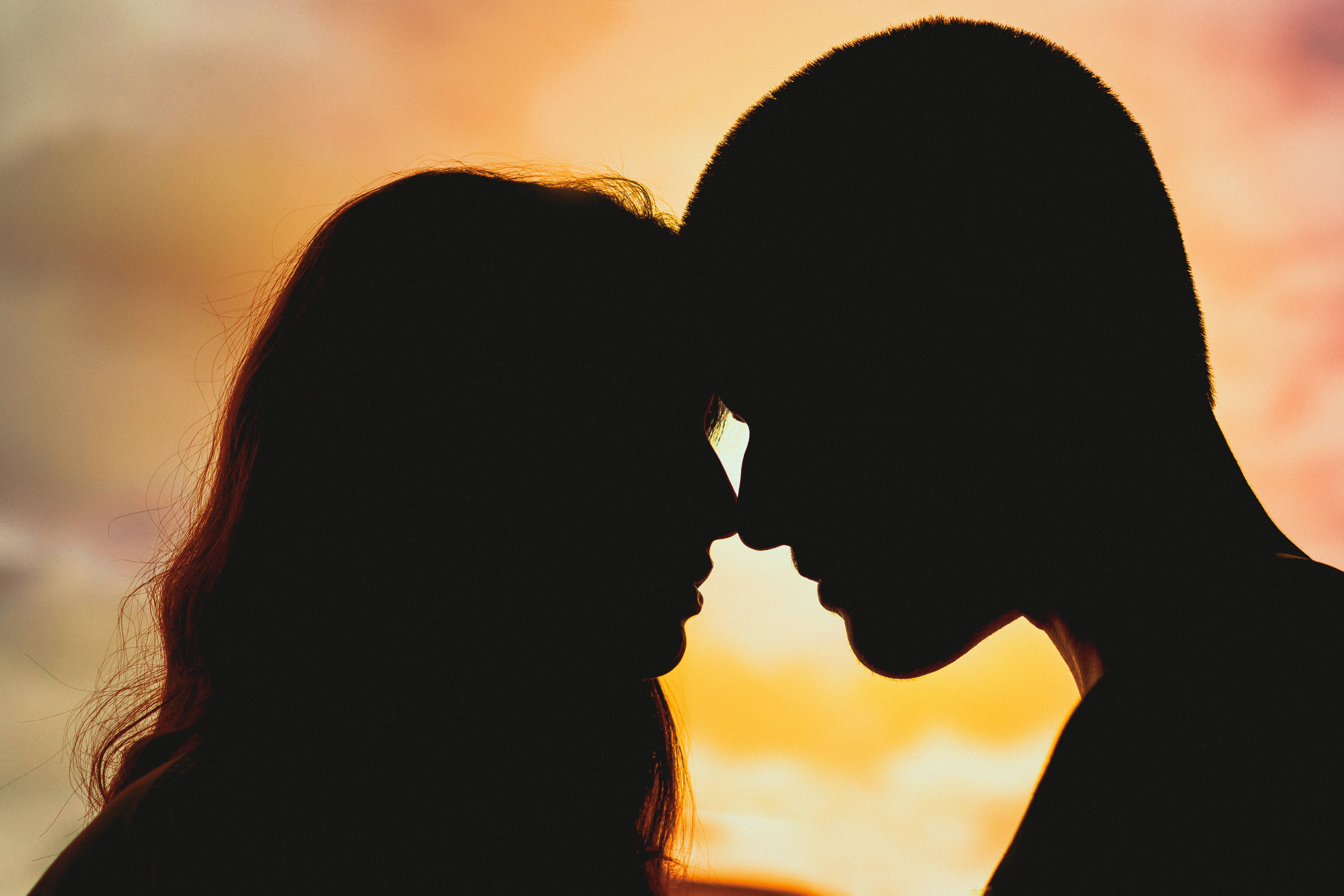 couple kiss 桌布 壁紙 — 一對情侶額頭相觸的剪影，背景是溫暖的日落天空和柔軟的雲朵。