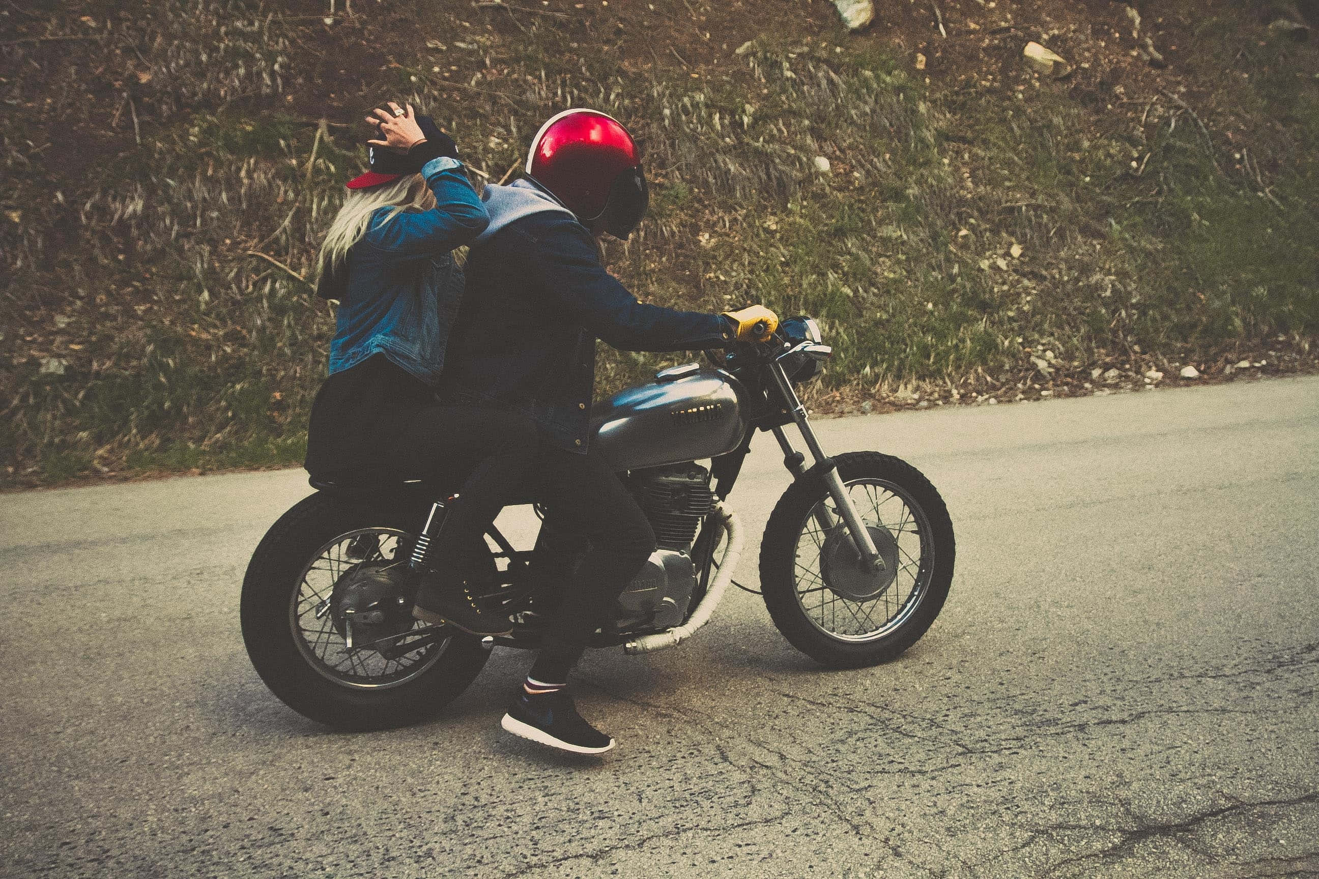 biker 桌布 壁紙 — 一對情侶騎著復古摩托車行駛在一條裂開的道路上，背景是長滿草的山坡。