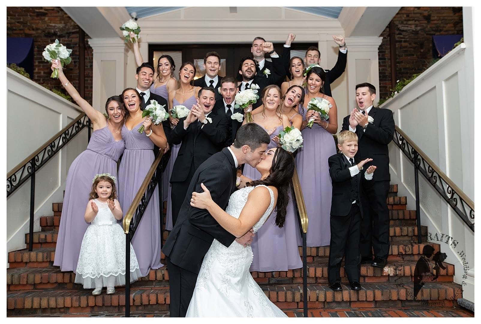 Bridal 桌布 壁紙 — 一對新人在大樓梯上親吻，周圍穿著正式服裝的賓客歡呼，一場歡樂的婚禮派對正在慶祝。