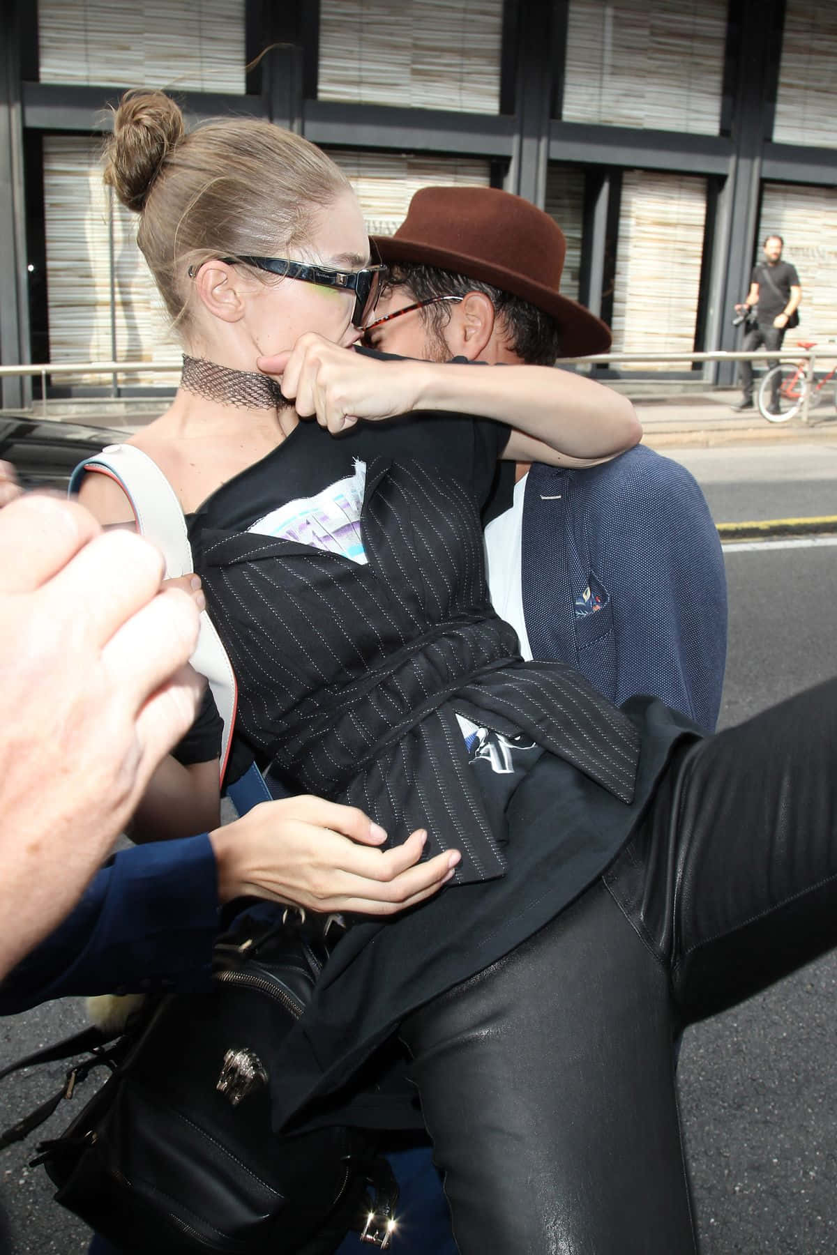 Celebrity 桌布 壁紙 — 一對時尚情侶在城市的街道上親密接吻，背景有現代建築和騎腳踏車的人。