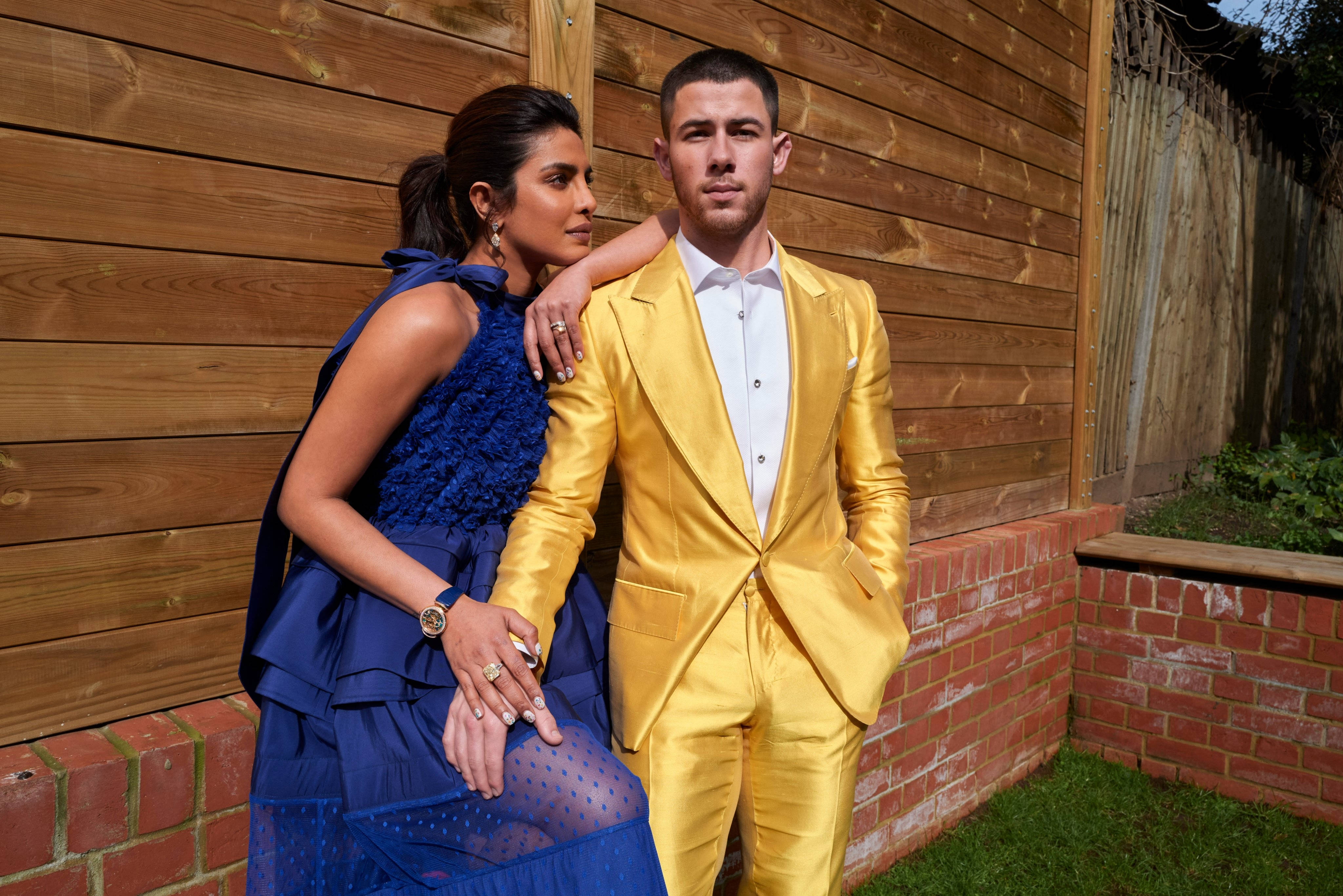 Priyanka 桌布 壁紙 — 一對時尚情侶在木柵欄前擺姿勢，女子身穿藍色衣服，男子身穿金色西裝。