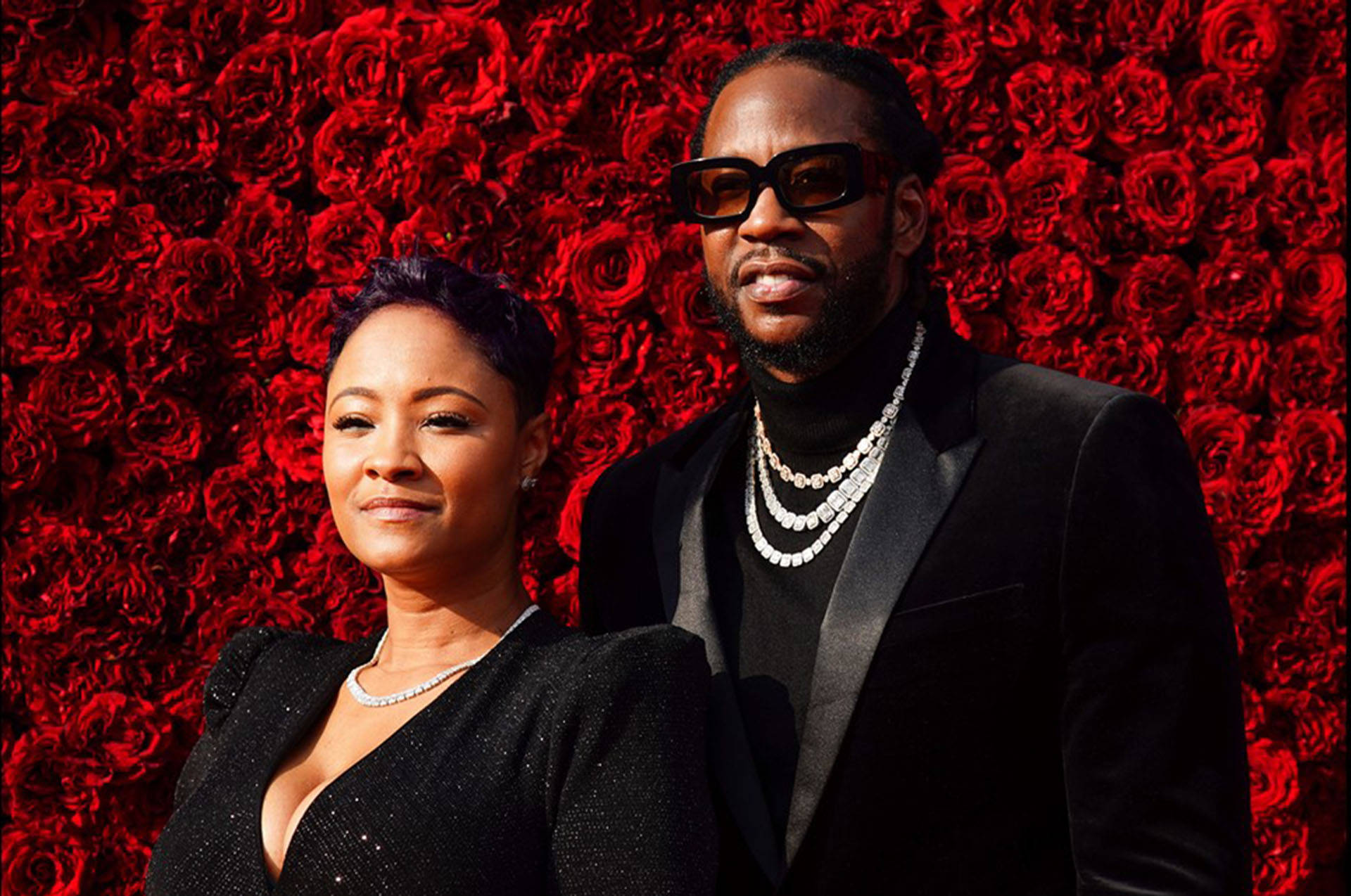 2 Chainz 桌布 壁紙 — 一對時尚情侶在鮮紅玫瑰牆背景下自信地擺姿勢。