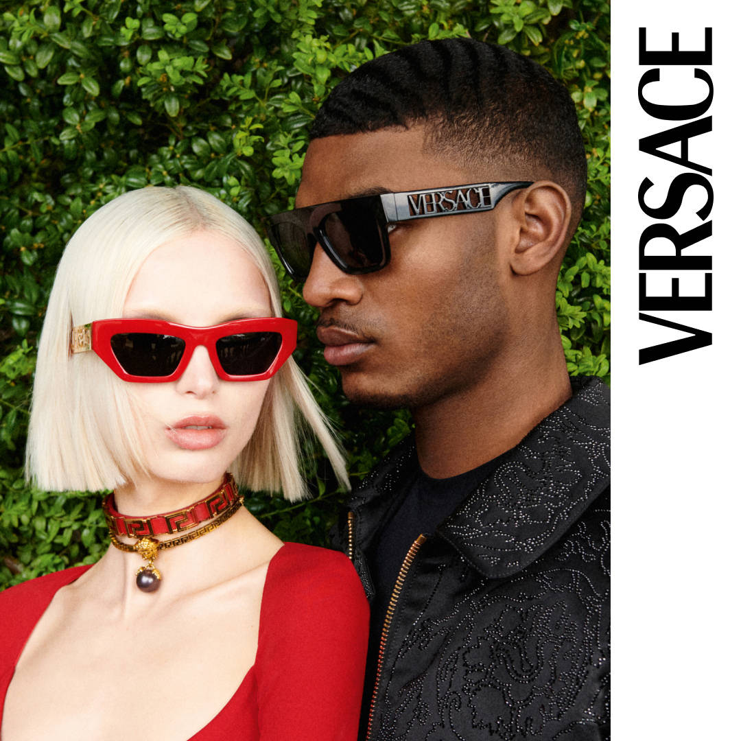 品牌 桌布 壁紙 — 一對時尚情侶戴著大膽的紅色和黑色 Versace 太陽眼鏡，在茂密的綠色樹籬背景下擺姿勢。
