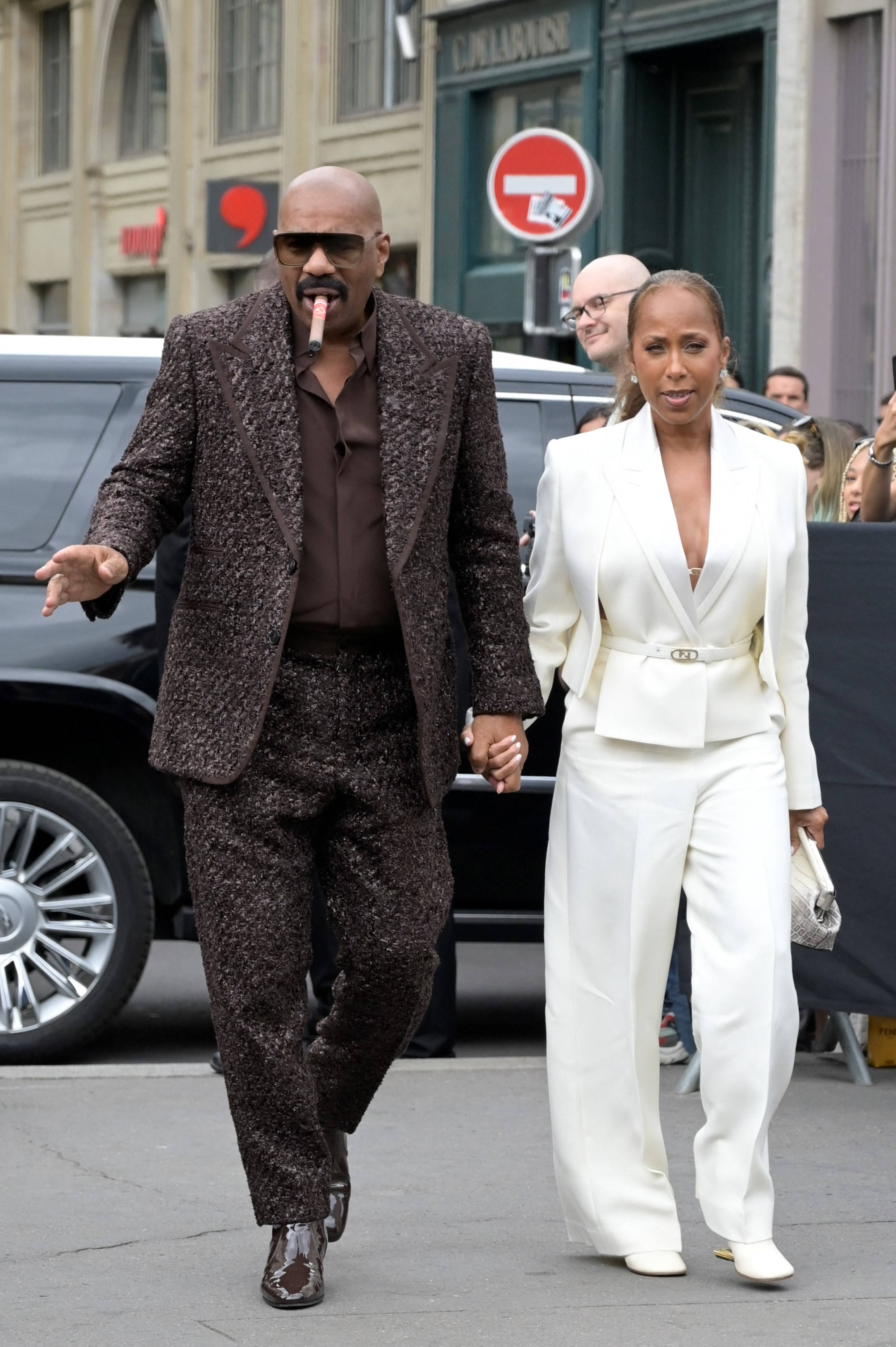 steve harvey 桌布 壁紙 — 一對時尚情侶手牽手走在城市街道上，背景有黑色SUV和商店門面。