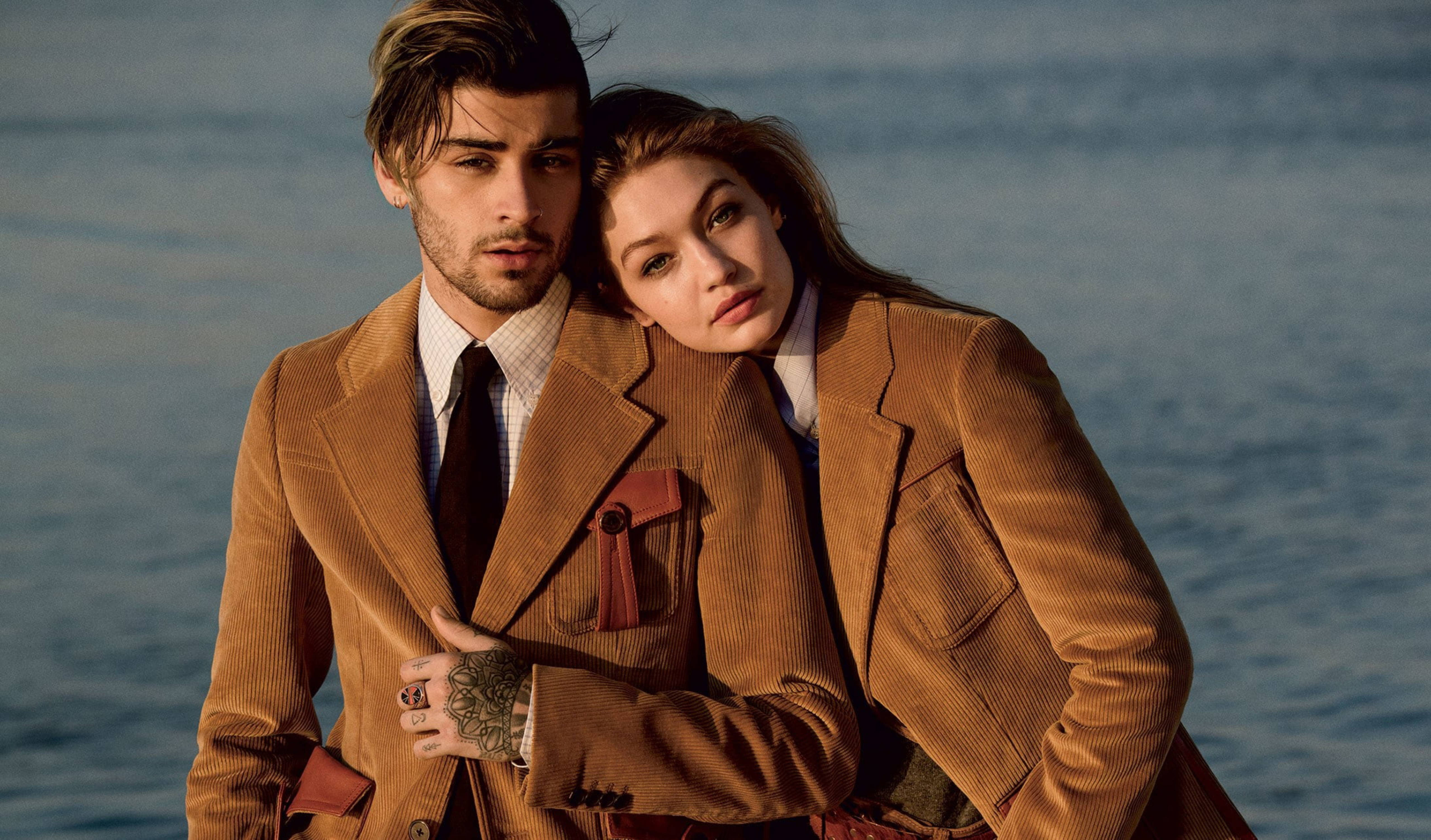 zayn 桌布 壁紙 — 一對時尚情侶穿著相配的棕色燈芯絨外套，在黃金時刻以平靜的海洋為背景親密擺姿勢。