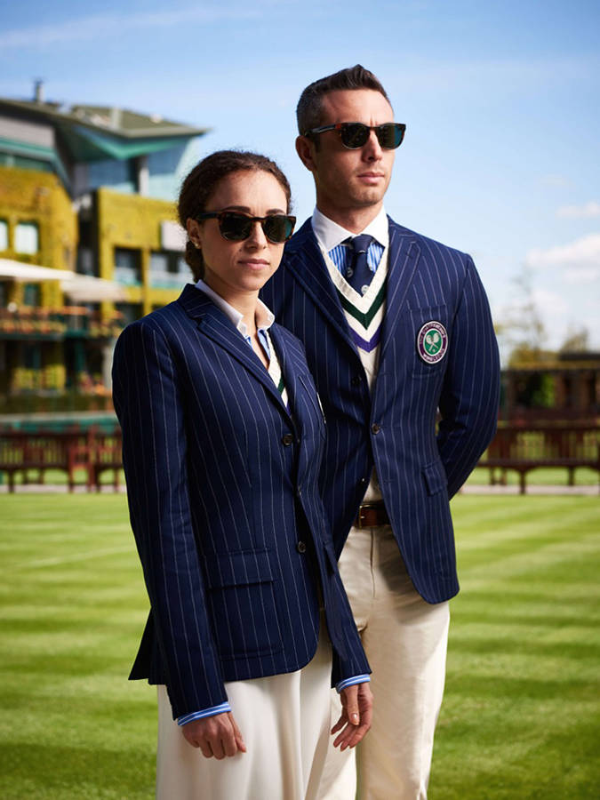ralph lauren 桌布 壁紙 — 一對時尚情侶身穿海軍藍細條紋西裝外套和太陽眼鏡，在晴朗的藍天下自信地站在修剪整齊的綠色草坪上。