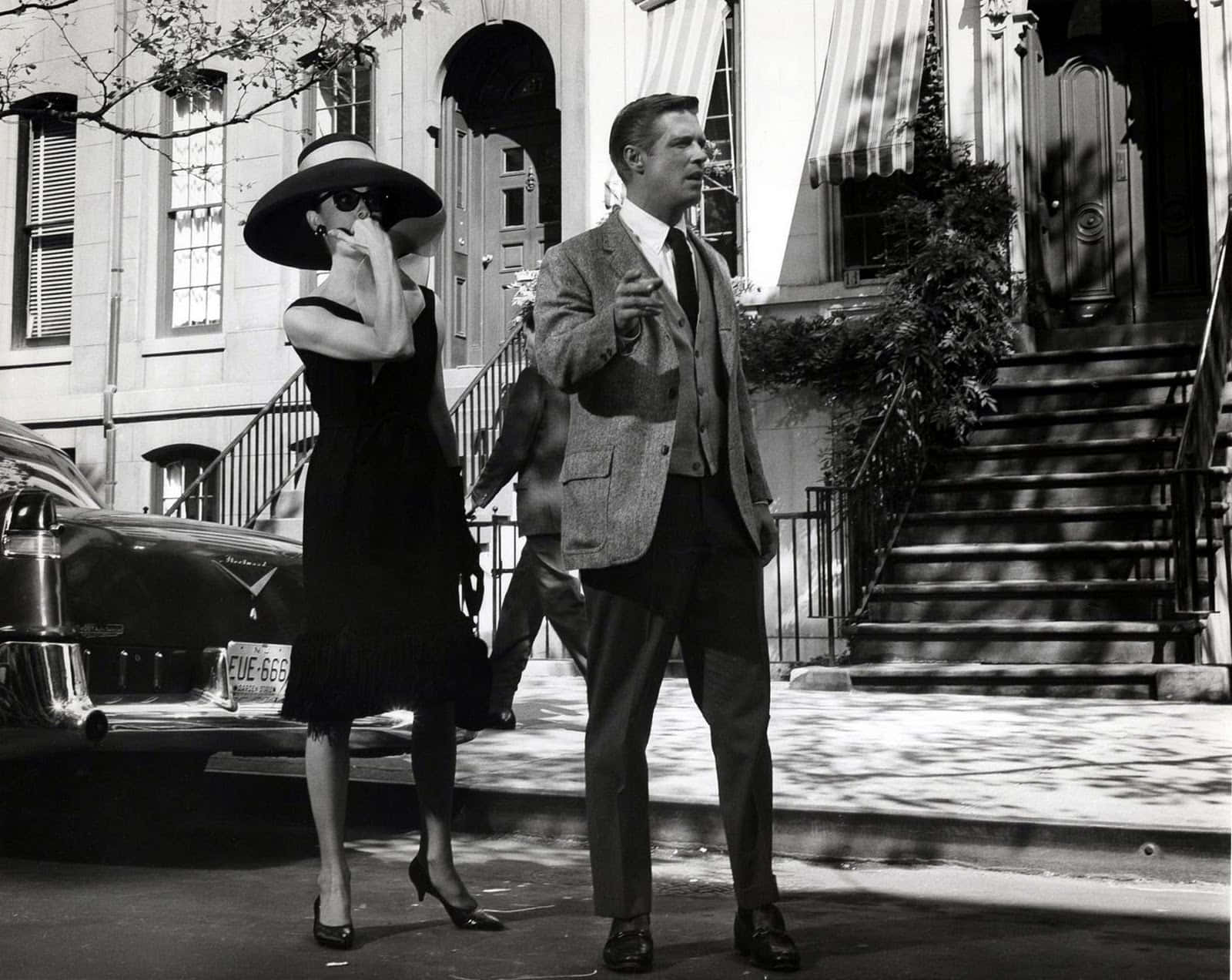actor 桌布 壁紙 — 一對時尚的1950年代情侶在陽光明媚的城市街道上漫步，經過經典汽車和階梯式房屋，以經典黑白呈現。