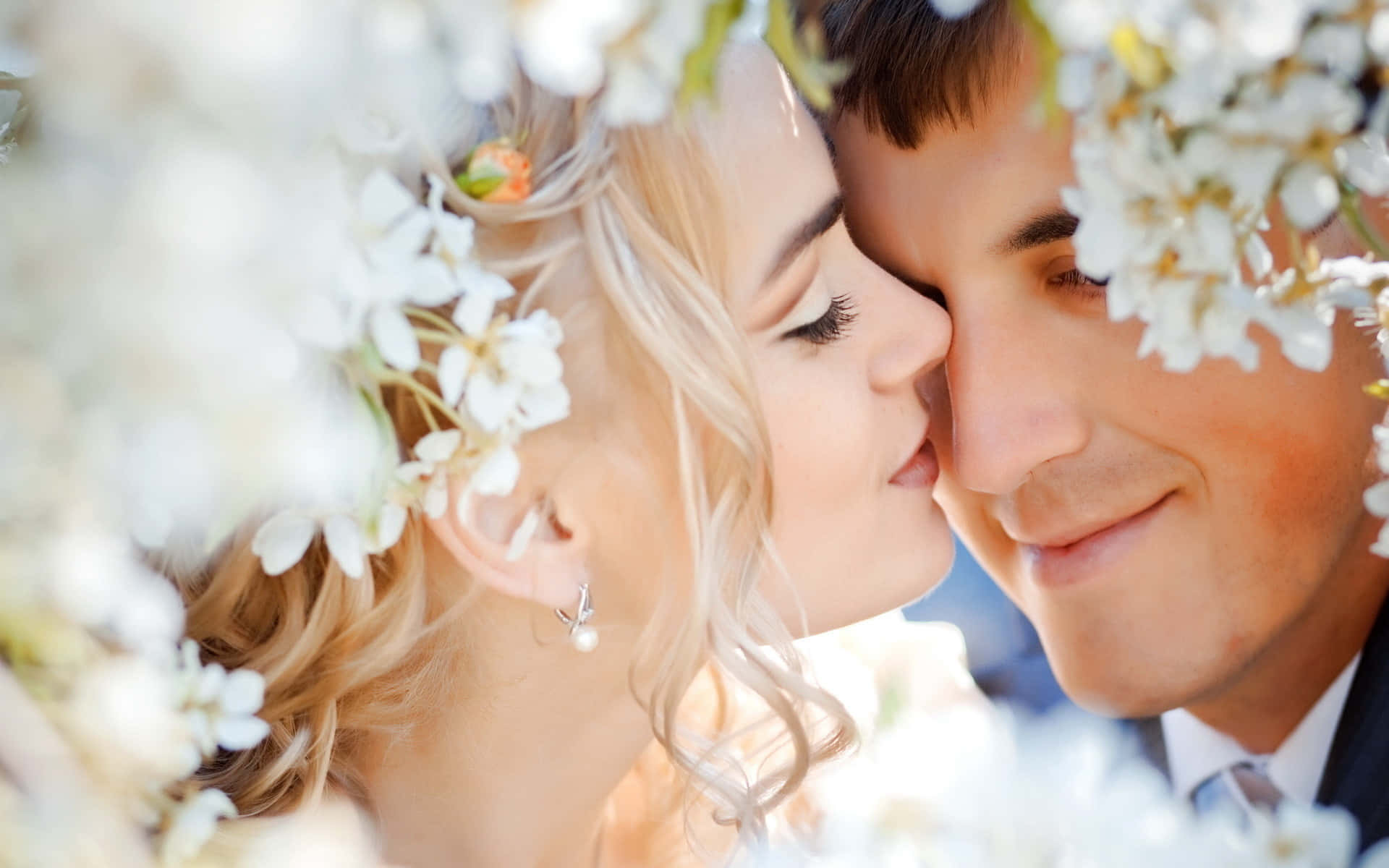 Wedding 桌布 壁紙 — 一對溫柔的情侶在明亮的日光下，被柔軟的白花環繞著親吻。