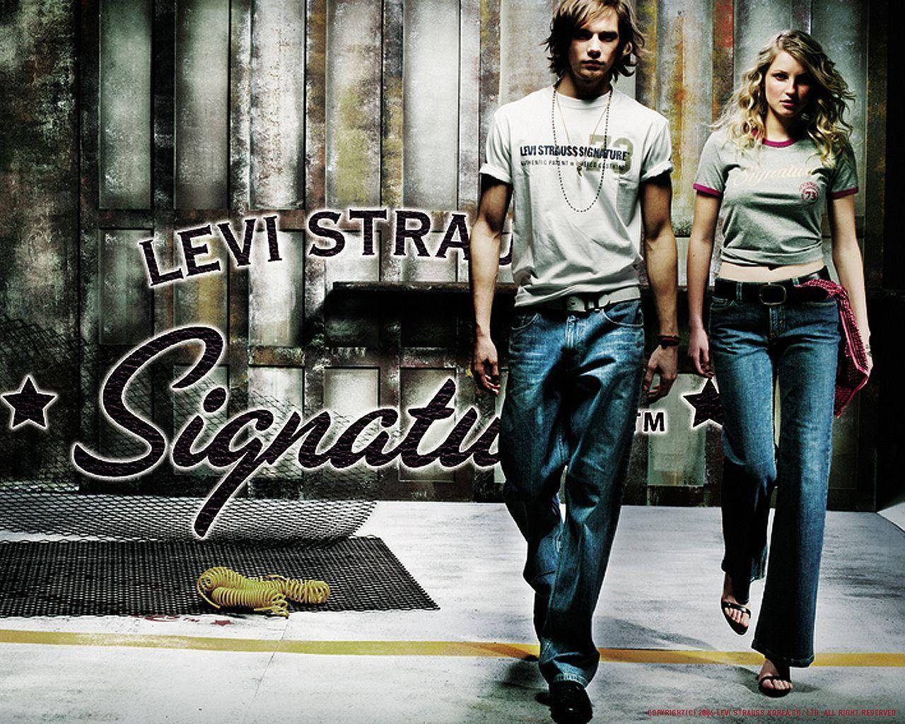 outfit 桌布 壁紙 — 一對男女穿著Levi's牛仔褲自信地走過一面帶有'Levi Strauss Signature'品牌標誌的風化金屬牆。
