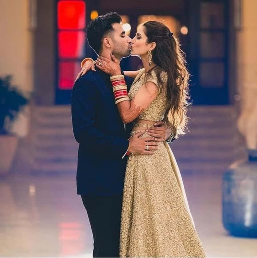 Kissing 桌布 壁紙 — 一對穿著傳統印度婚禮服飾的情侶在溫暖燈光的室內環境中親吻。