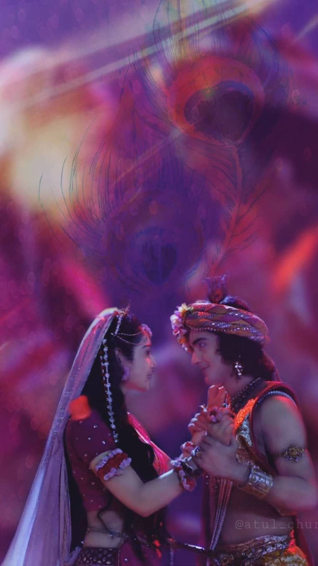 radha krishna serial 桌布 壁紙 — 一對穿著傳統印度服飾的情侶，在發光的孔雀羽毛下，以鮮豔的紫色和橙色背景，分享親密的目光。