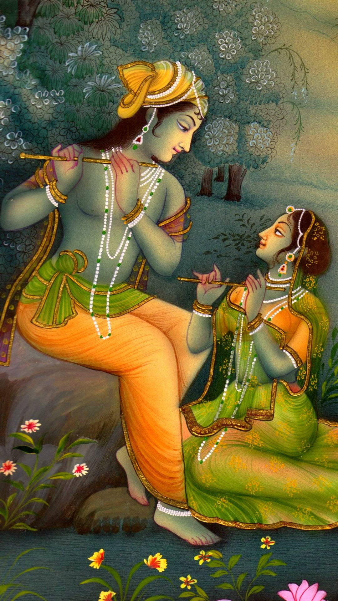 krishna iPhone 桌布 壁紙 — 一對穿著傳統印度服飾的神聖情侶在盛開的樹下一起吹奏長笛，場景寧靜如花園。
