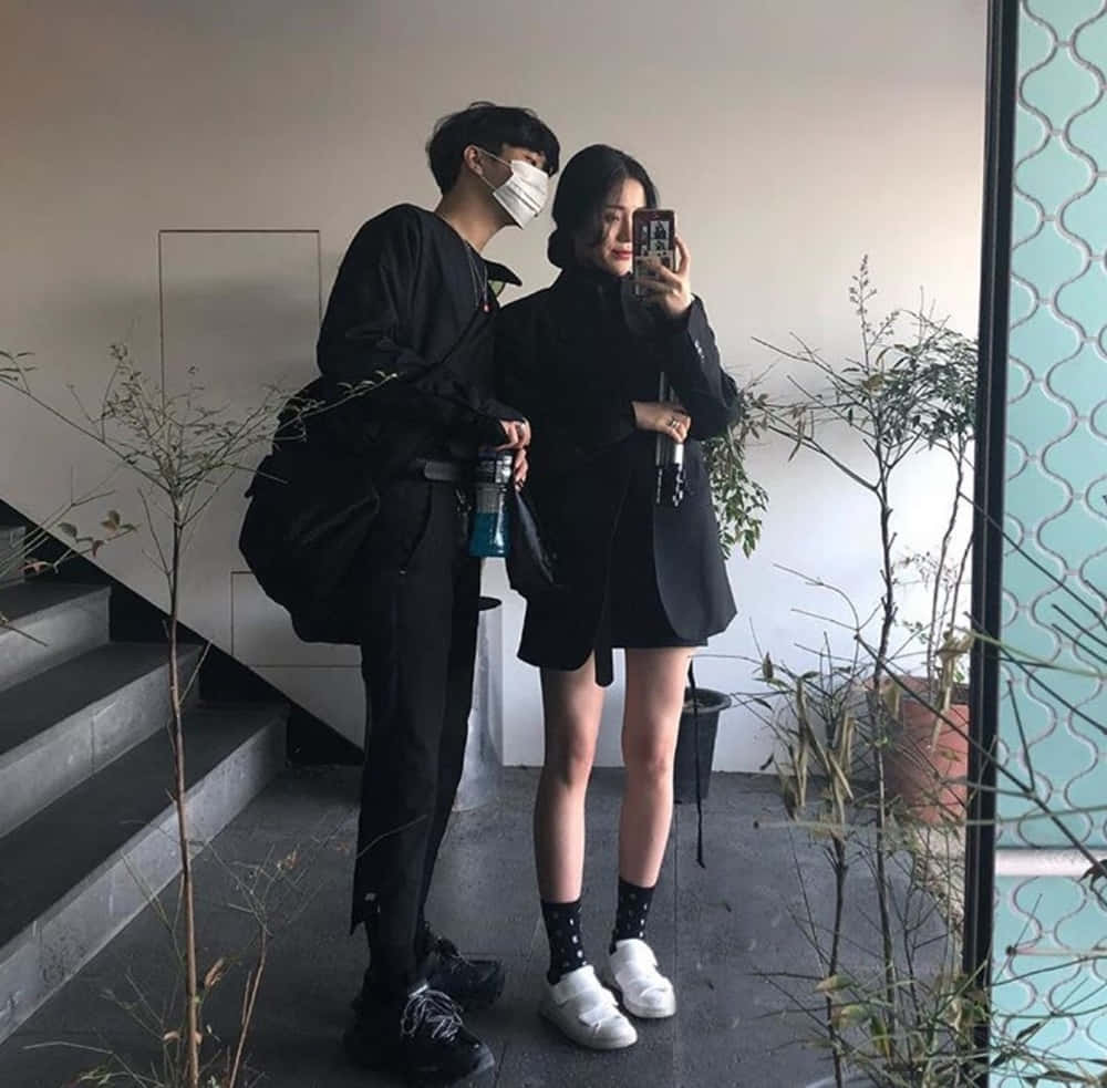 情侶 桌布 壁紙 — 一對穿著全黑服裝的情侶在室內以植物和樓梯為背景拍攝鏡子自拍照。