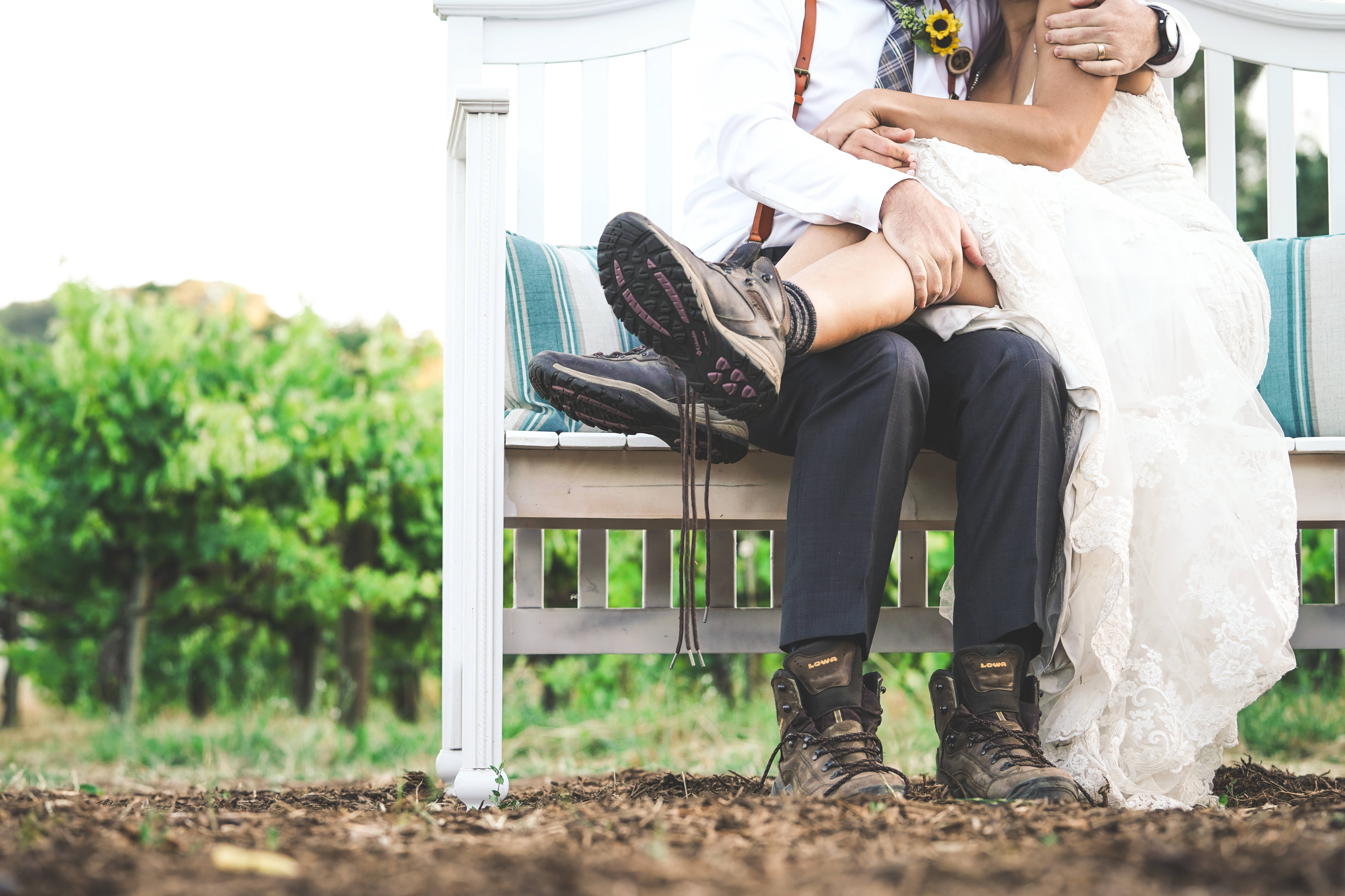 Groom 桌布 壁紙 — 一對穿著婚禮服飾的新娘和新郎親密地坐在葡萄園的白色長椅上，他們的登山靴與浪漫的場景形成對比。
