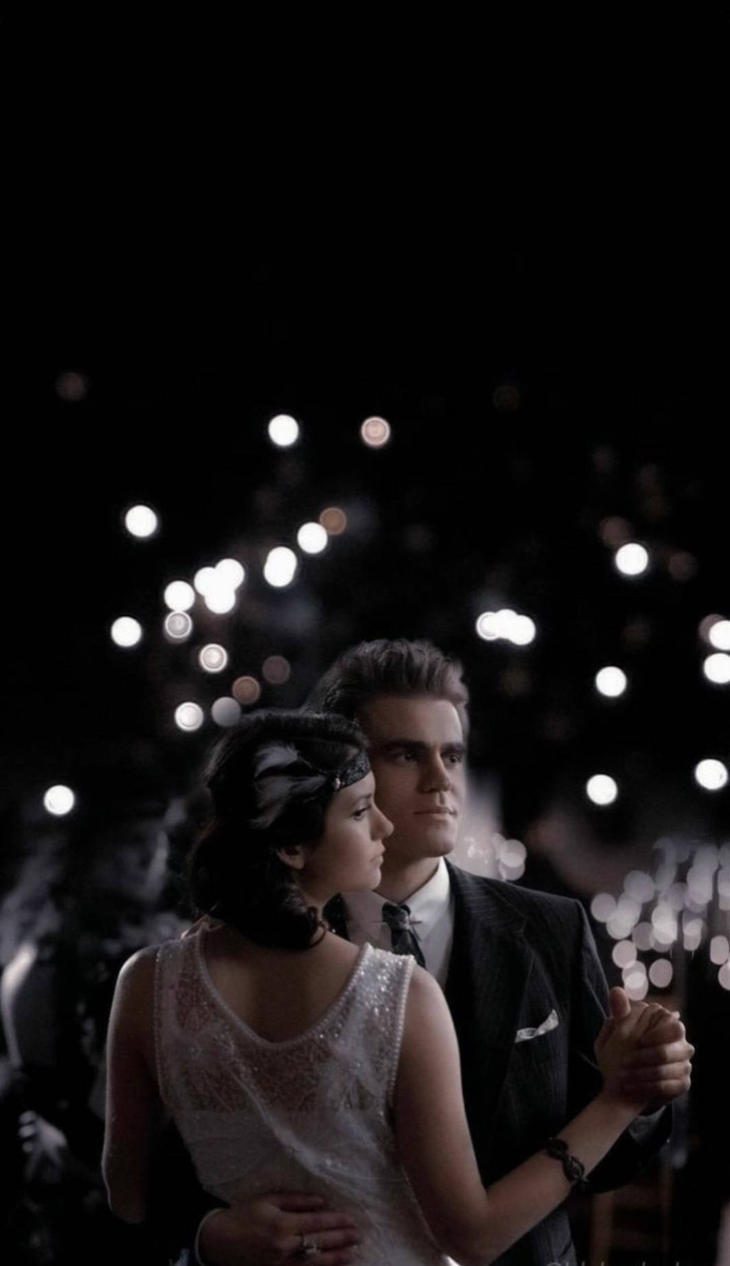 Vampire Diaries 桌布 壁紙 — 一對穿著復古服裝的情侶在黑暗夜空下閃爍的散景燈光中跳舞。