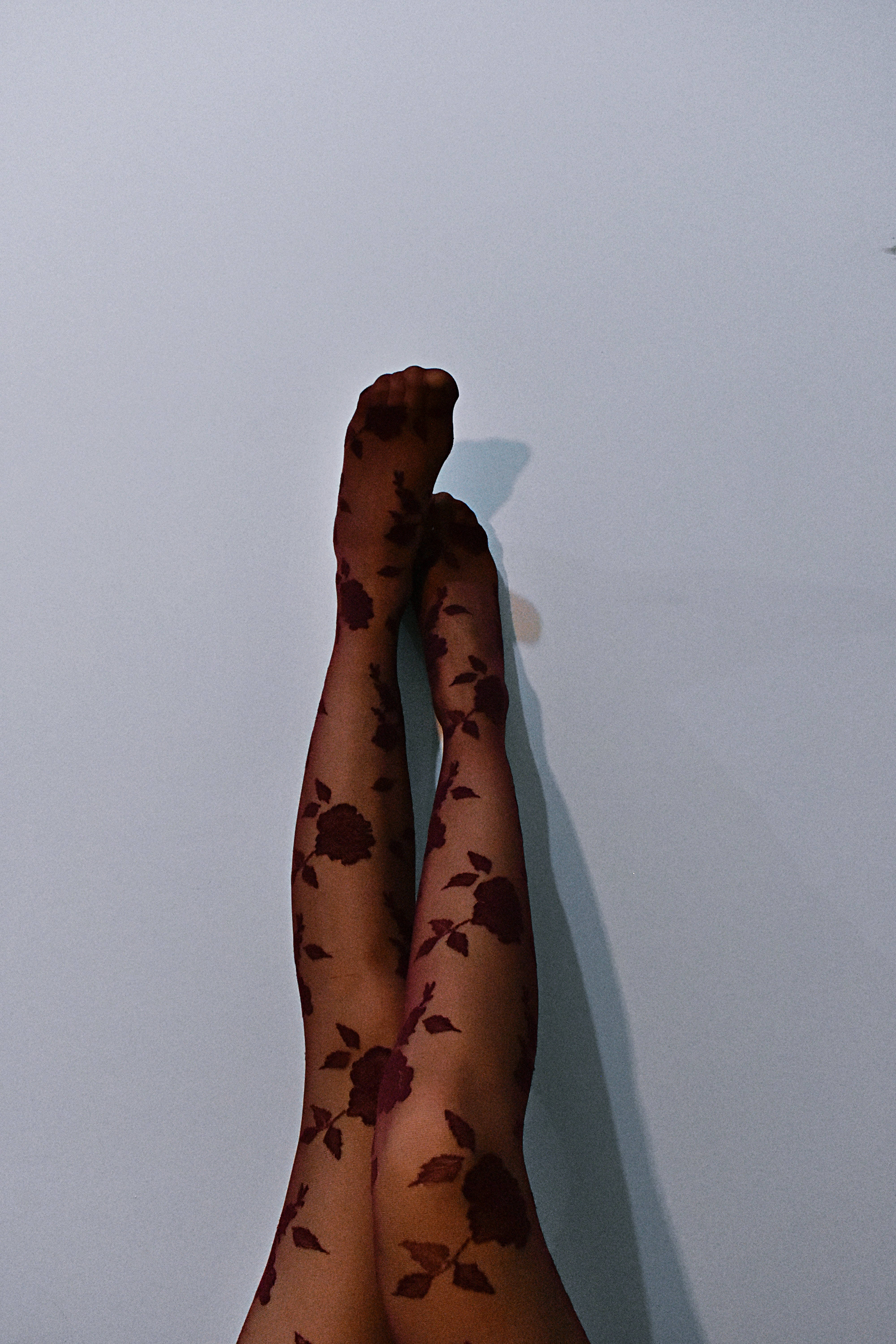 leggings 桌布 壁紙 — 一對穿著深色花卉圖案緊身褲的腿掛在純淺灰色牆上，投下柔和的陰影。
