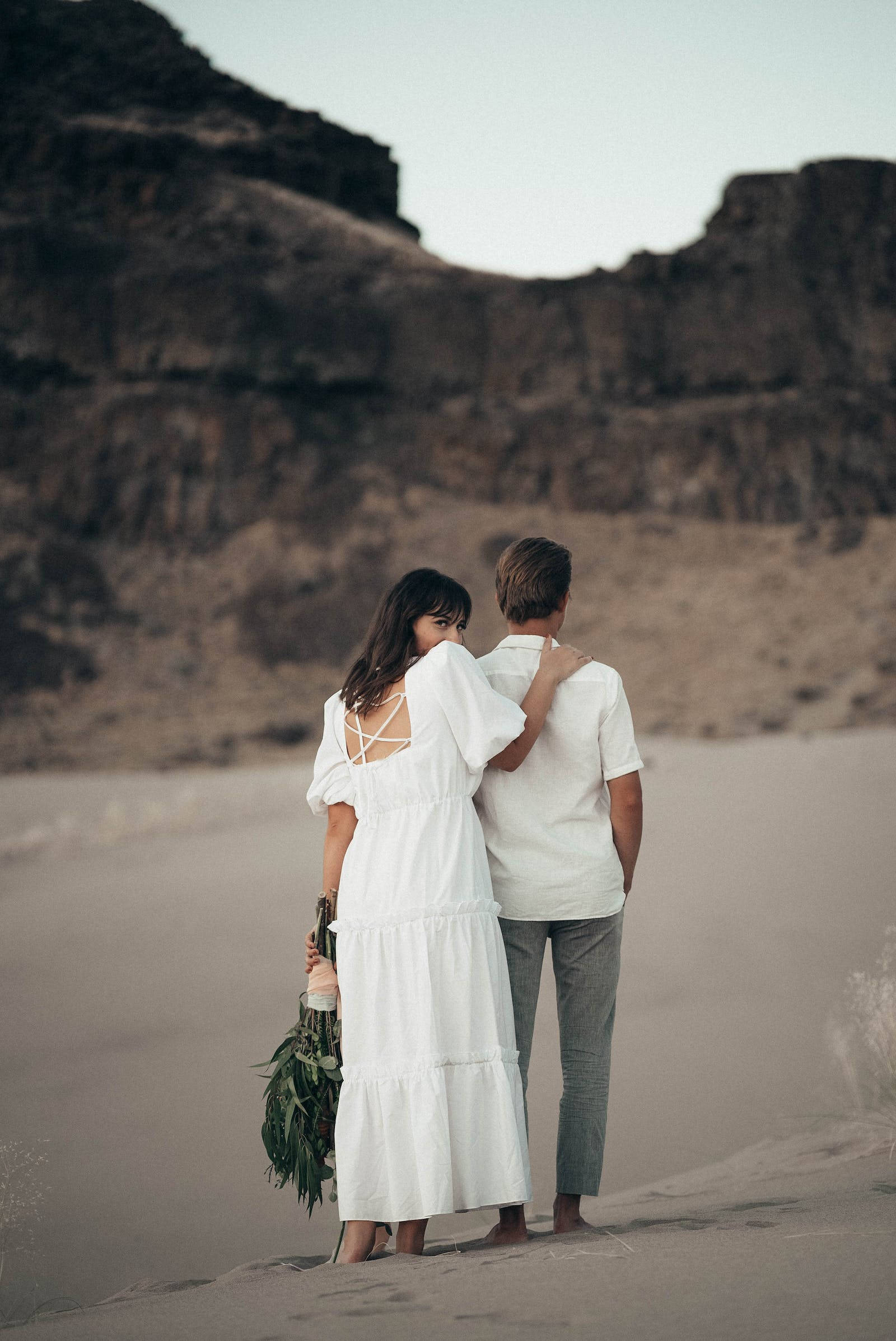 love full HD 桌布 壁紙 — 一對穿著白色衣服的情侶在金色時刻的沙丘上擁抱，身後是崎嶇的懸崖。