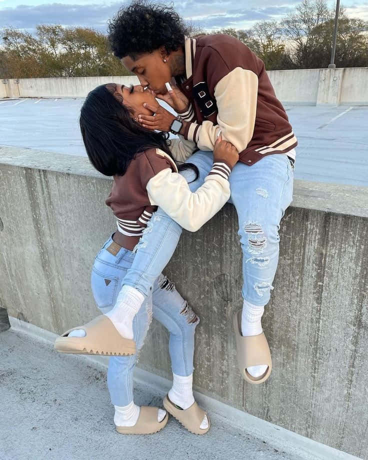Matching Couple Profile 桌布 壁紙 — 一對穿著相配棒球外套的情侶在黃昏的混凝土屋頂上熱情接吻。