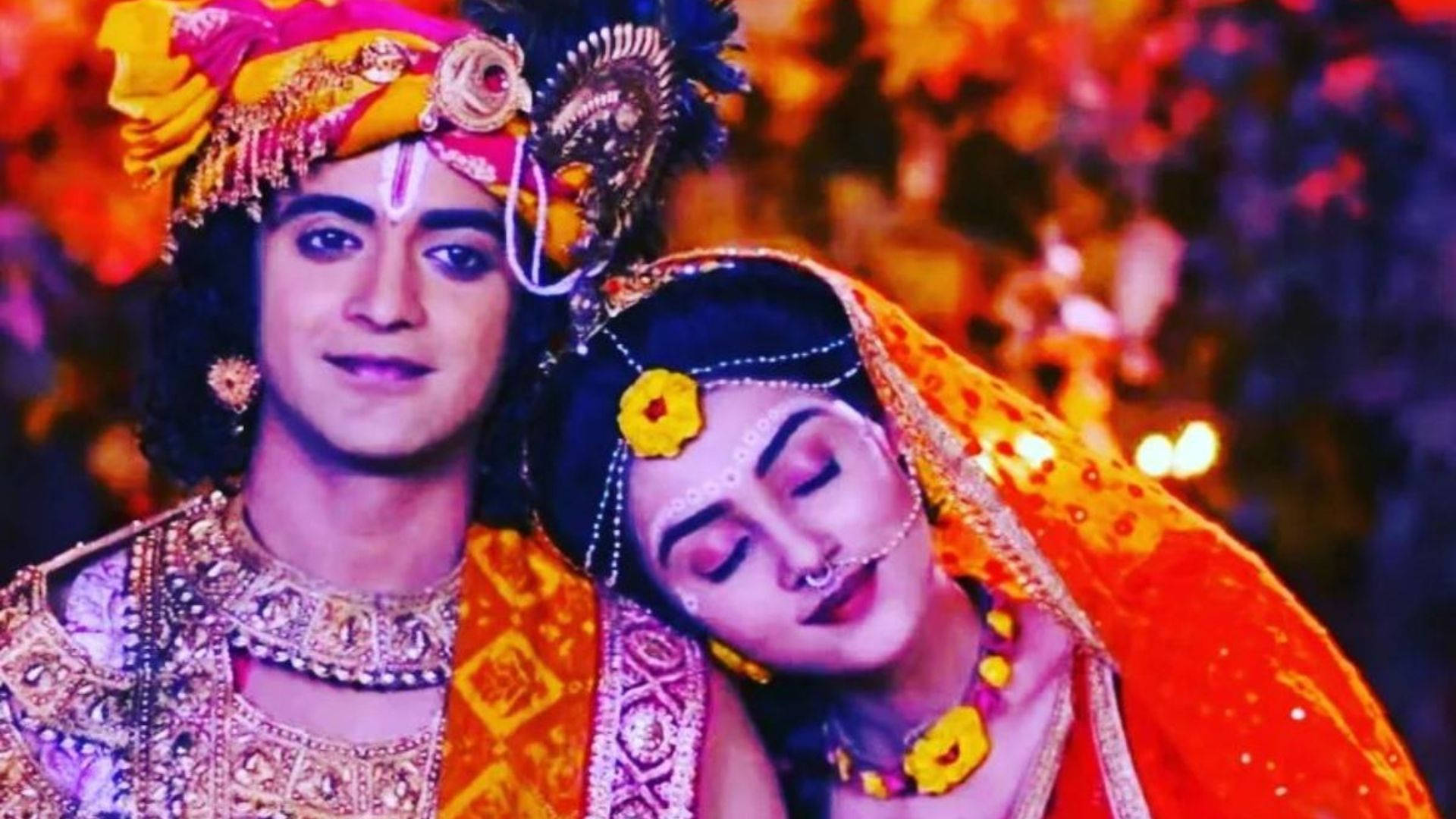 radha krishna serial 桌布 壁紙 — 一對穿著華麗傳統印度婚禮服飾的情侶，在充滿活力的花卉背景下溫暖地擁抱。