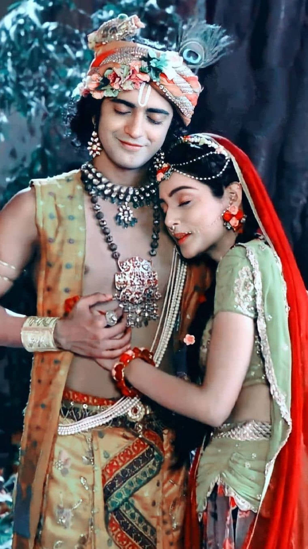 radha krishna serial 桌布 壁紙 — 一對穿著華麗傳統印度服飾的情侶在翠綠的樹叢中溫柔擁抱。