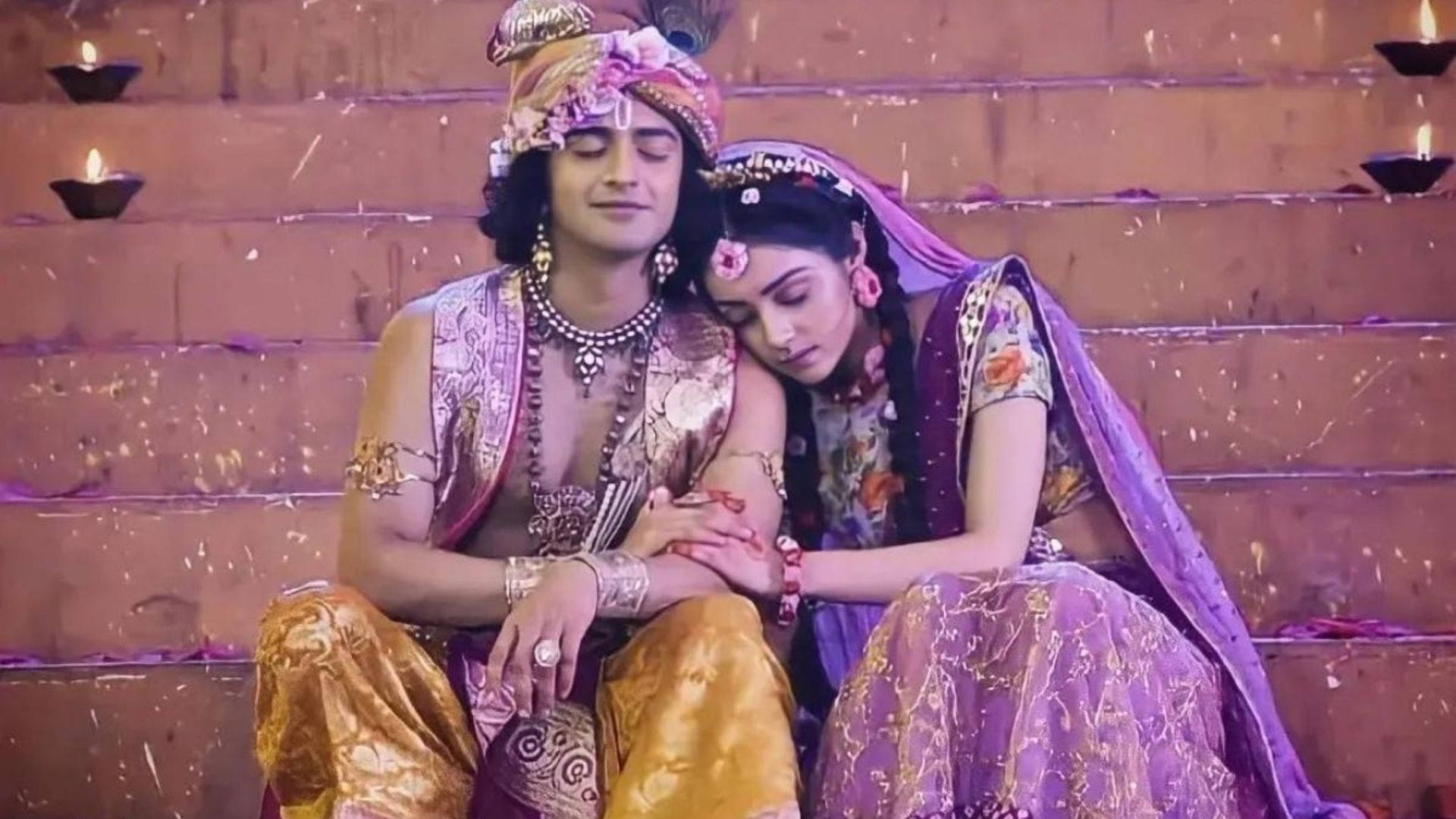radha krishna serial 桌布 壁紙 — 一對穿著華麗傳統印度服飾的情侶親密地坐在石階上，石階上點綴著點燃的油燈和飄落的花瓣。