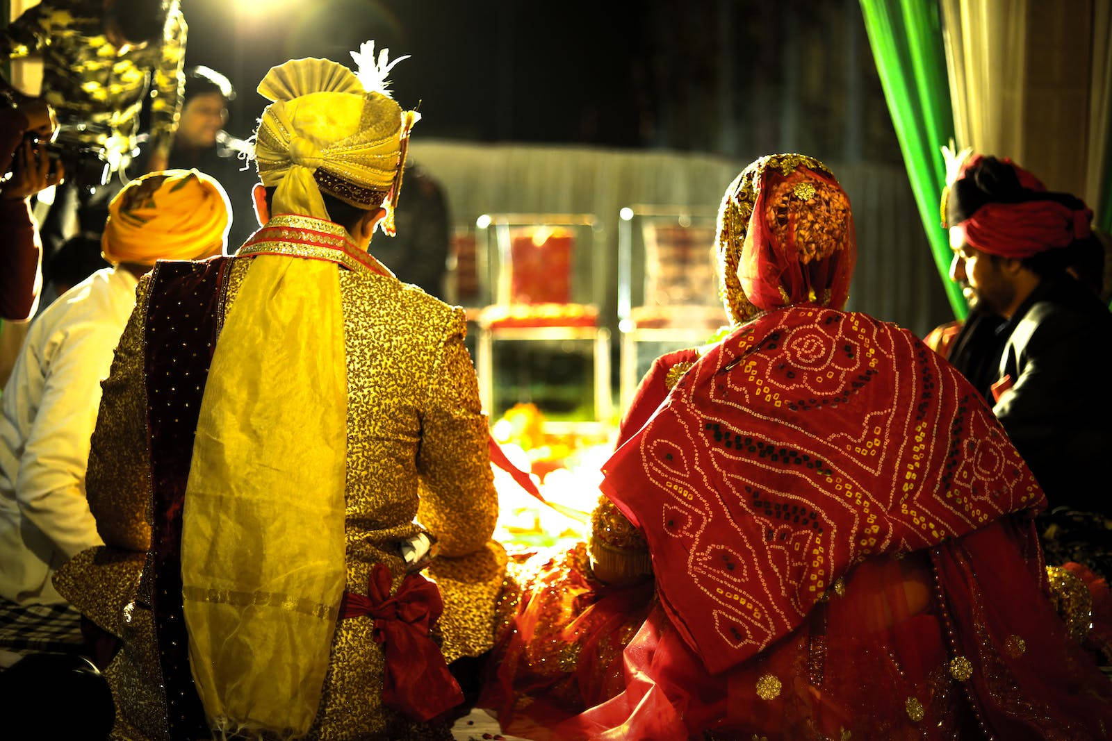 Indian 桌布 壁紙 — 一對穿著華麗傳統婚禮服飾的夫婦，在夜間溫暖的舞台燈光下，面對著儀式火堆而坐。