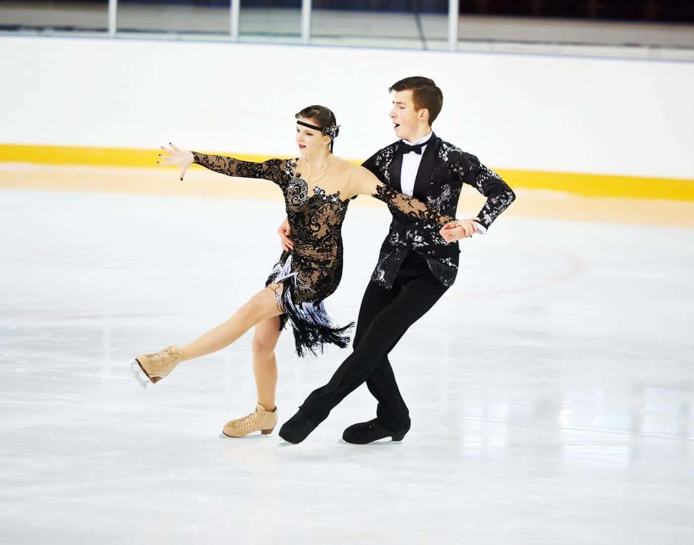 figure skating 桌布 壁紙 — 一對穿著黑色蕾絲服裝的花式滑冰雙人組在表演期間優雅地滑過冰場。