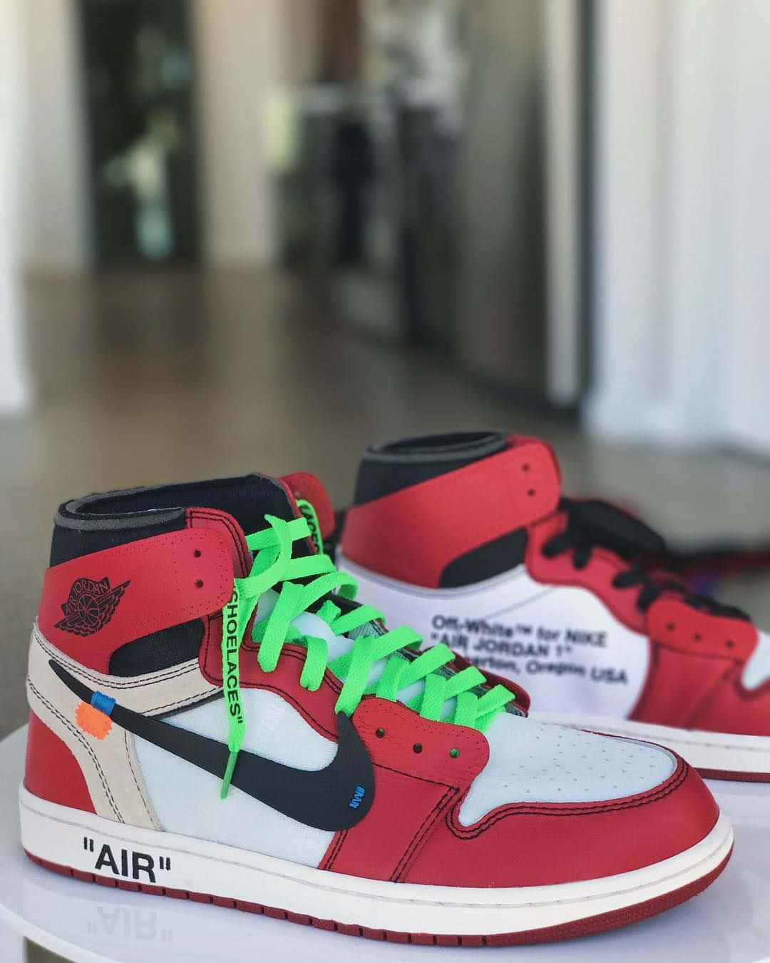 Off White Jordan 1 桌布 壁紙 — 一對紅白黑色的 Off White x Nike Air Jordan 1 運動鞋，搭配螢光綠色鞋帶，展示在白色底座上。