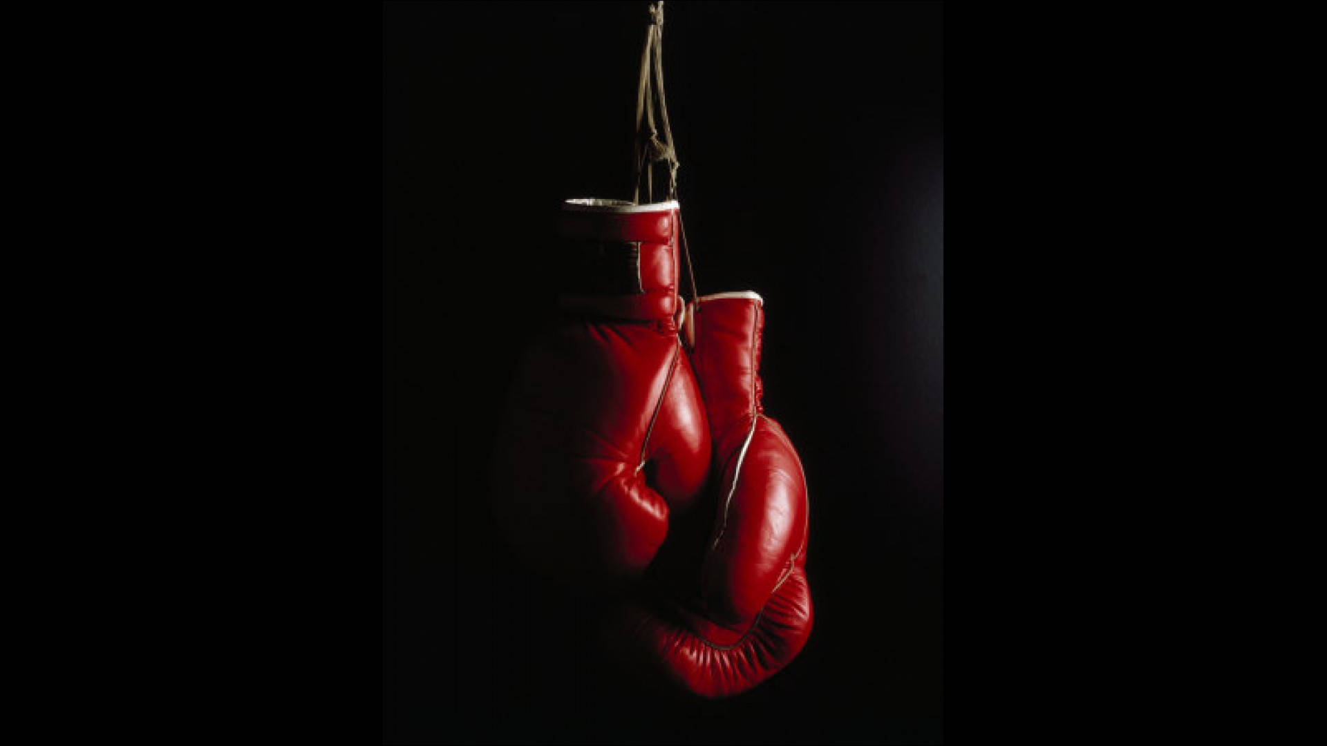 Cool Boxing 桌布 壁紙 — 一對紅色拳擊手套懸掛在純黑色背景上，由戲劇性的側光照亮。