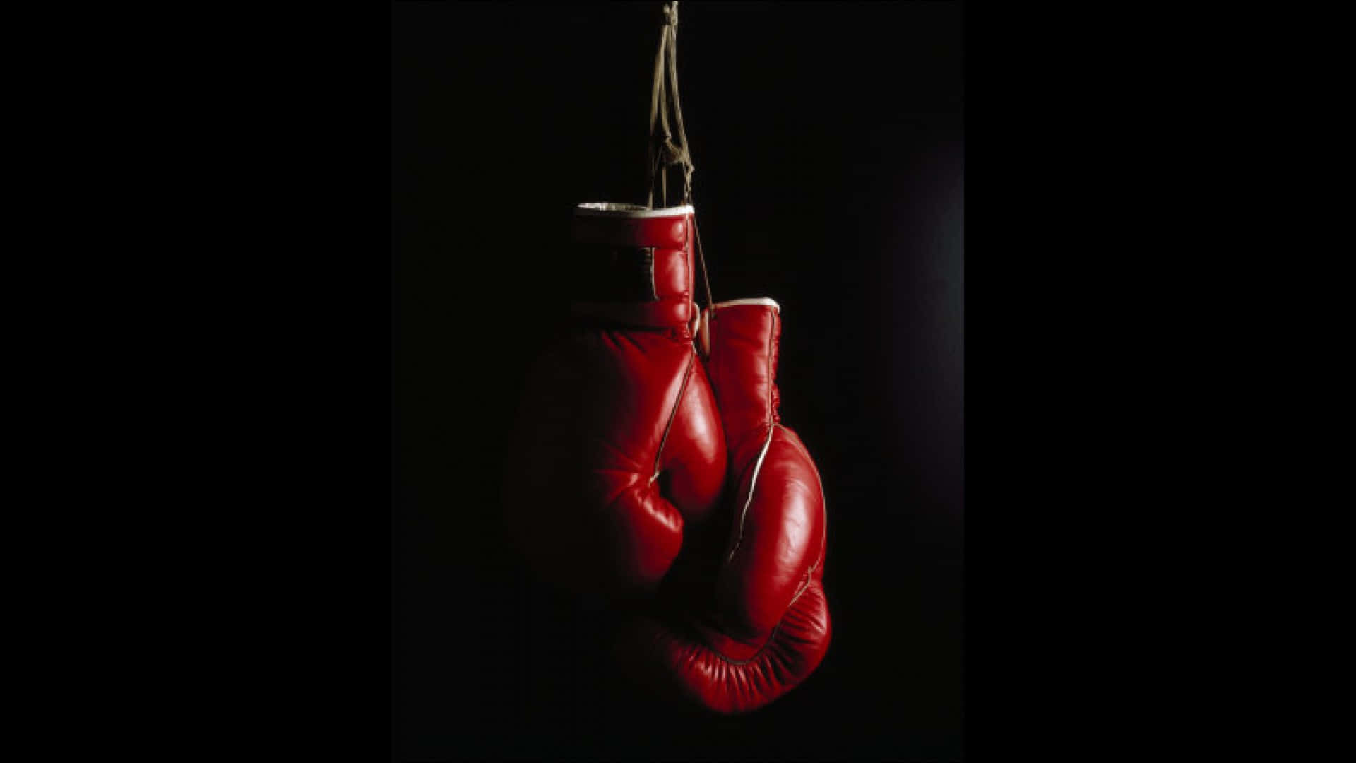 Boxing 桌布 壁紙 — 一對紅色拳擊手套懸掛在黑色背景上，由戲劇性的側光照亮。