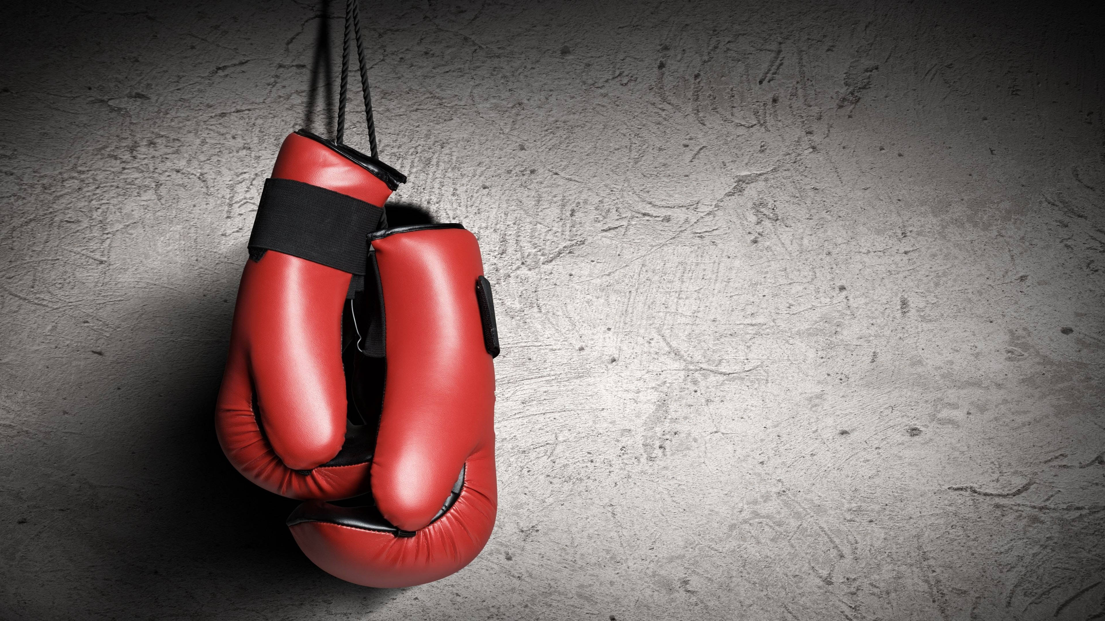 Cool Boxing 桌布 壁紙 — 一對紅色拳擊手套用黑色繩帶掛在帶有紋理的灰色混凝土牆上，在戲劇性的聚光燈下。