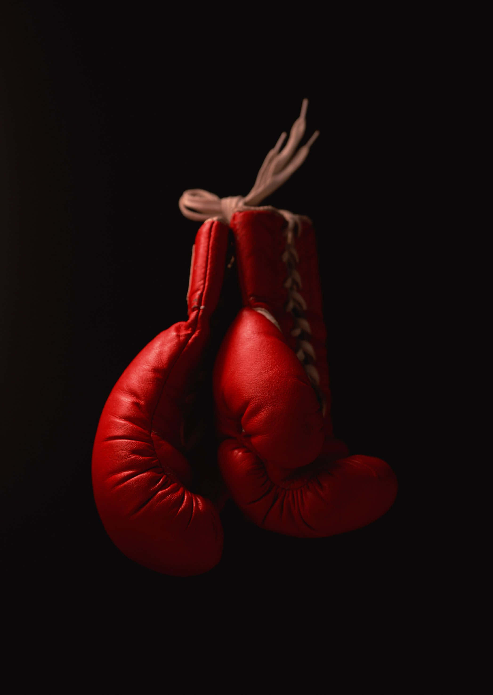Boxing 桌布 壁紙 — 一對紅色皮製拳擊手套懸掛在純黑色背景前，由戲劇性的燈光照亮。