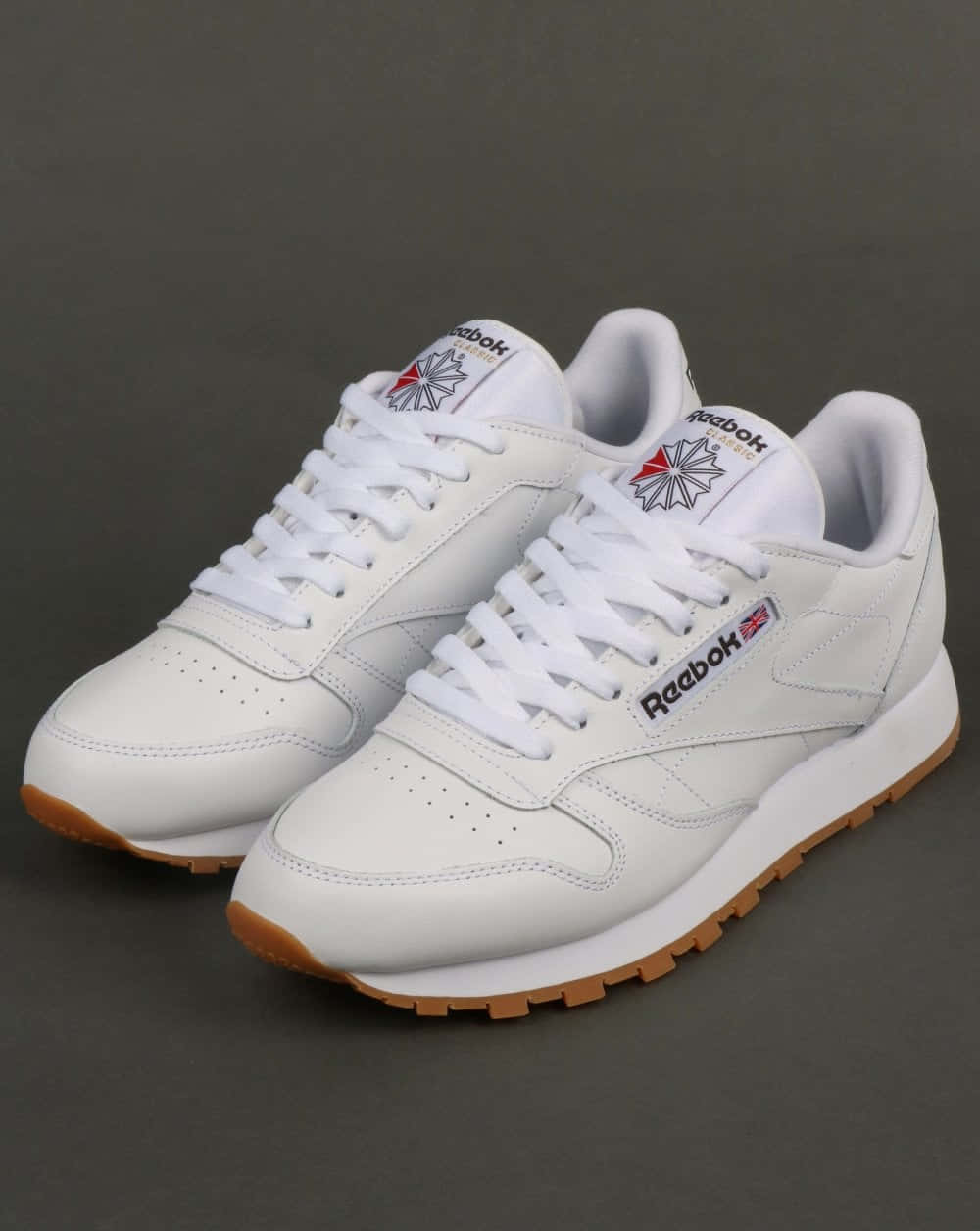 銳步 桌布 壁紙 — 一對純白Reebok Classic運動鞋搭配橡膠鞋底，整齊地斜放在深灰色工作室背景上。