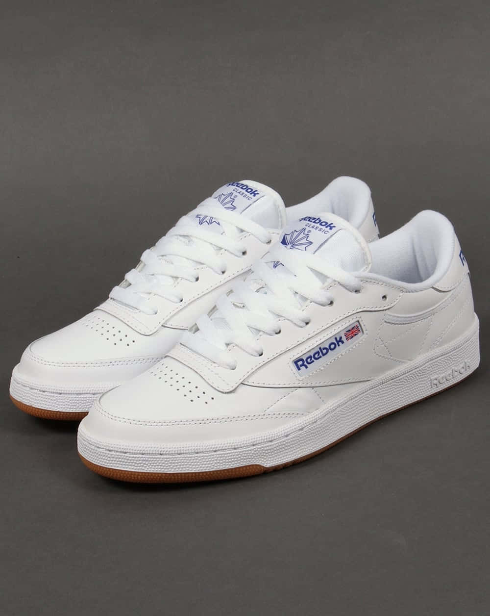 Reebok 桌布 壁紙 — 一對純白色Reebok Classic運動鞋，帶有藍色品牌標誌和橡膠鞋底，在灰色中性工作室背景下拍攝。