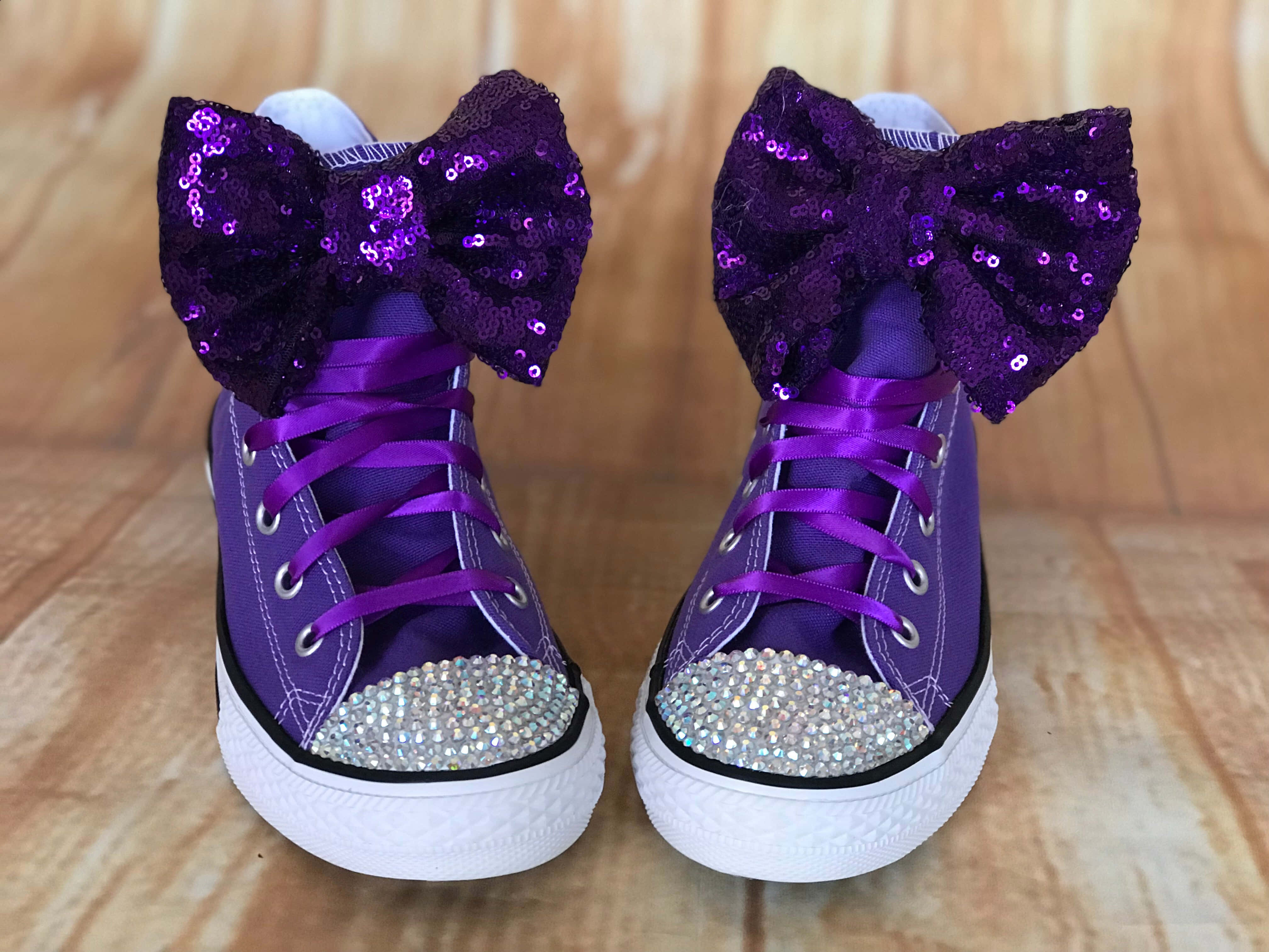 Purple Shoes 桌布 壁紙 — 一對紫色高筒運動鞋，帶有亮粉蝴蝶結和水鑽鞋頭，放在木地板上。