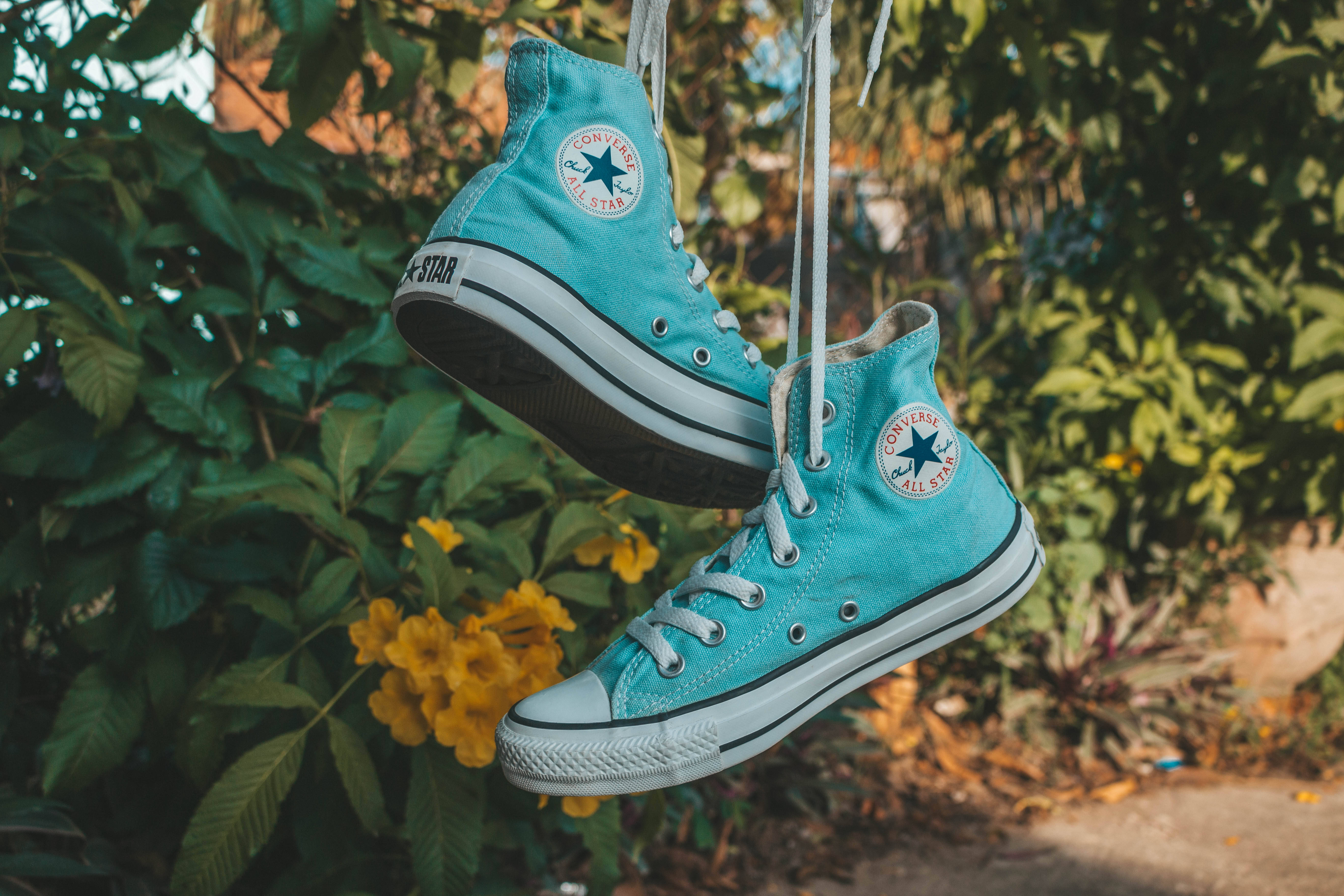 Converse 桌布 壁紙 — 一對綠松色Converse運動鞋掛在鞋帶上，背景是茂密的綠色樹葉和鮮黃色的花朵。