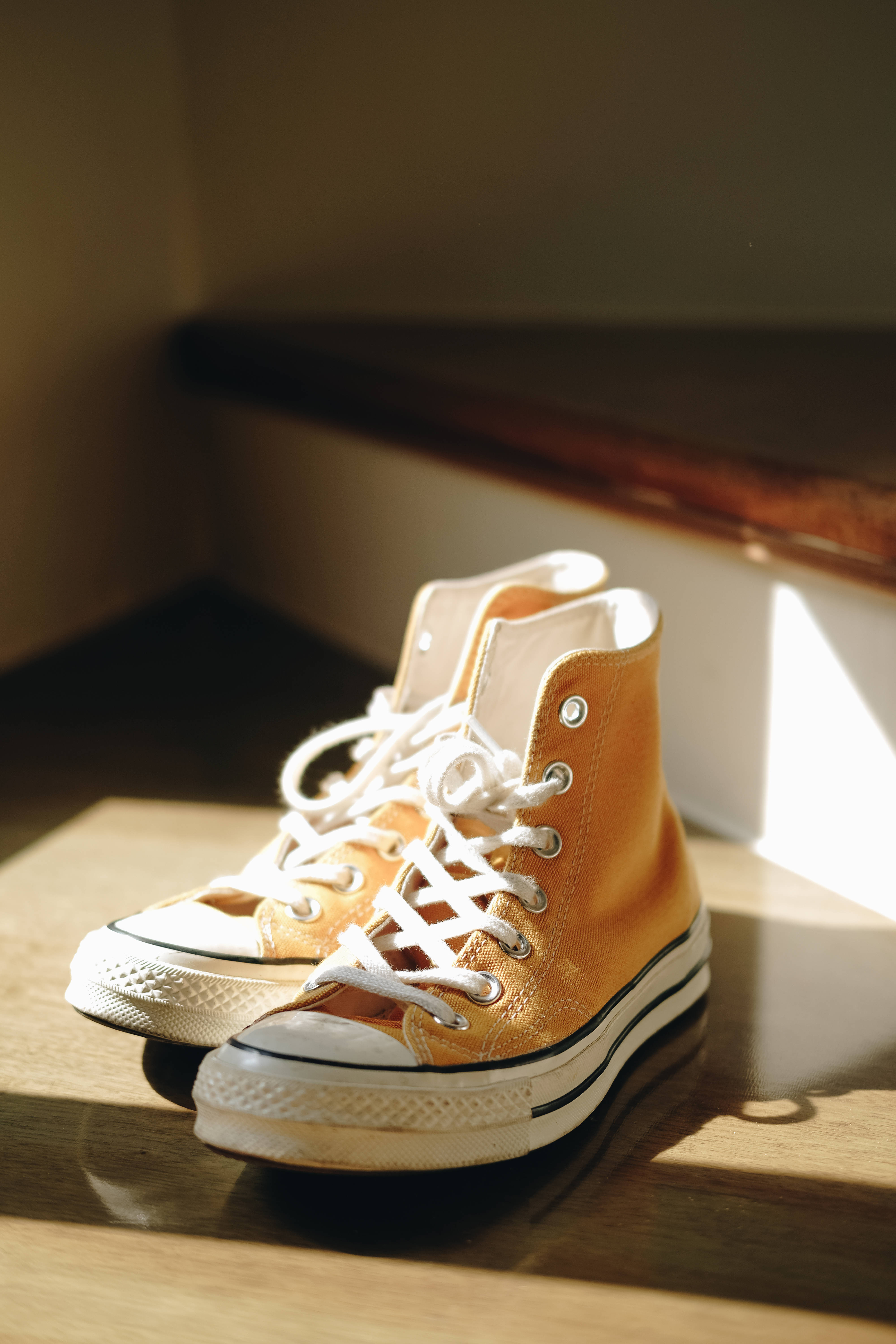 Converse 桌布 壁紙 — 一對芥末黃色高筒運動鞋搭配白色鞋帶，擱在溫暖陽光灑落的木地板上。