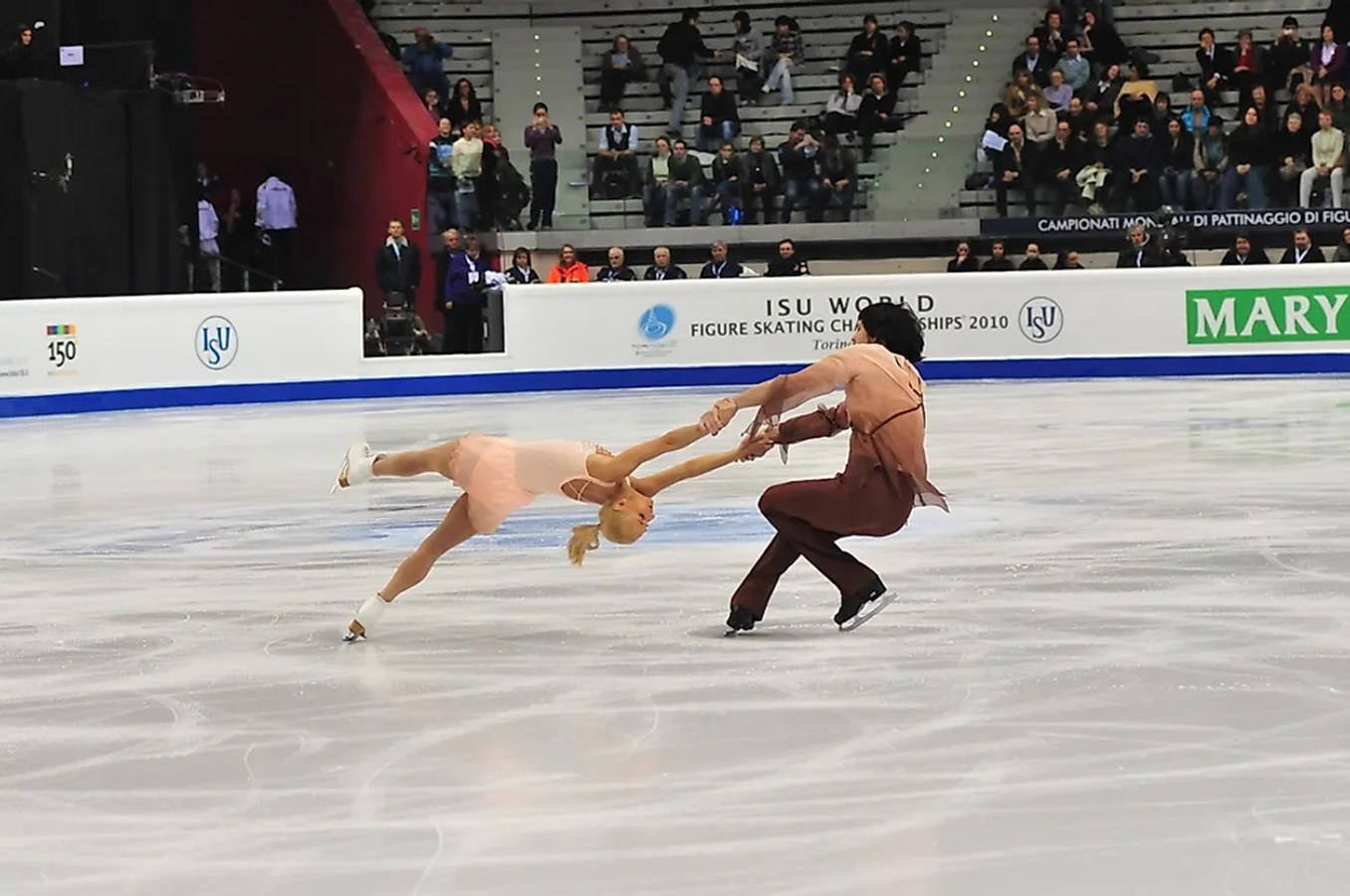 Olympics 桌布 壁紙 — 一對花式滑冰選手在2010年世界錦標賽中執行一個動態的托舉，觀眾從階梯式座位觀看。