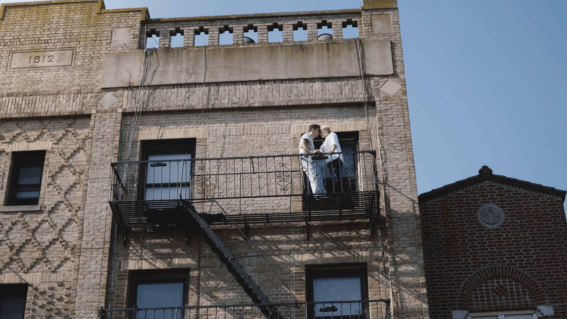 Love Story 桌布 壁紙 — 一對身穿白色婚紗的情侶在風化磚砌建築的防火梯上，在晴朗的藍天下接吻。