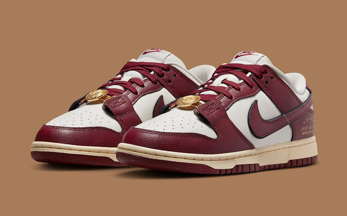 Nike 桌布 壁紙 — 一對酒紅色和白色的 Nike Dunk Low 運動鞋，帶有金幣裝飾，置於純棕色背景上。