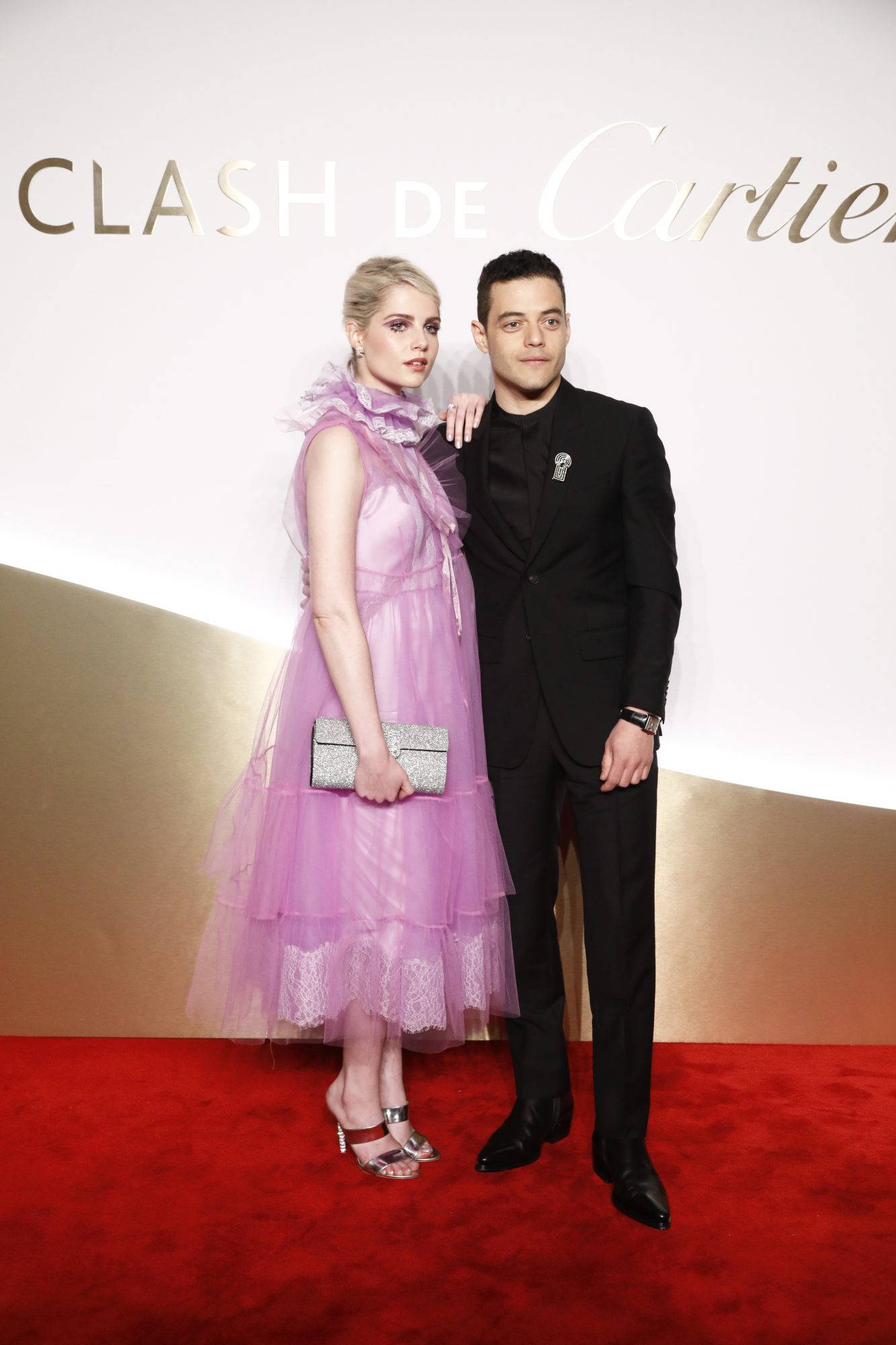 Rami Malek 桌布 壁紙 — 一對魅力情侶在卡地亞活動的金色和白色背景前於紅地毯上擺姿勢。