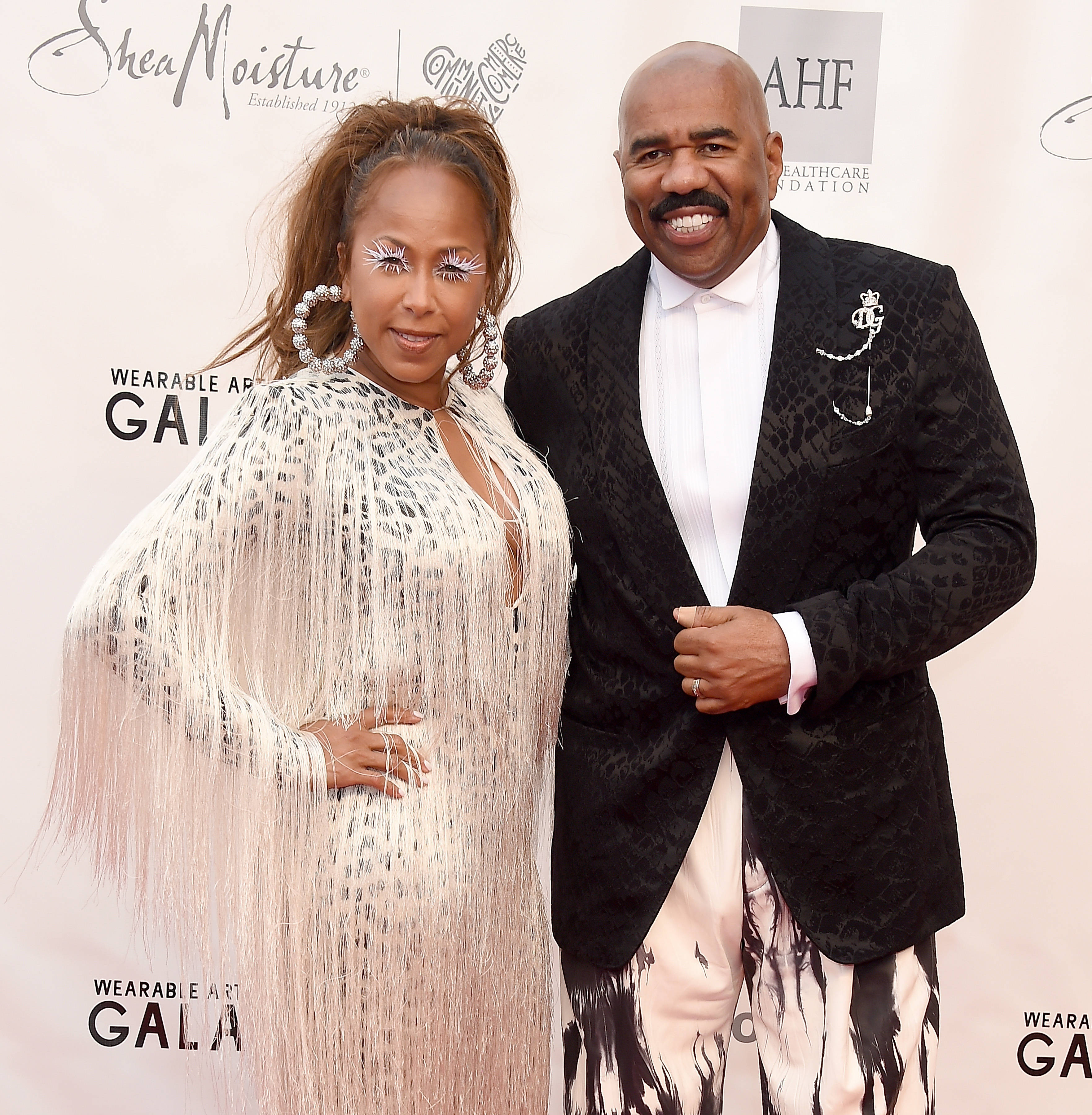 steve harvey 桌布 壁紙 — 一對魅力情侶在可穿戴藝術晚會的紅地毯上擺姿勢，展現大膽時尚和燦爛笑容。