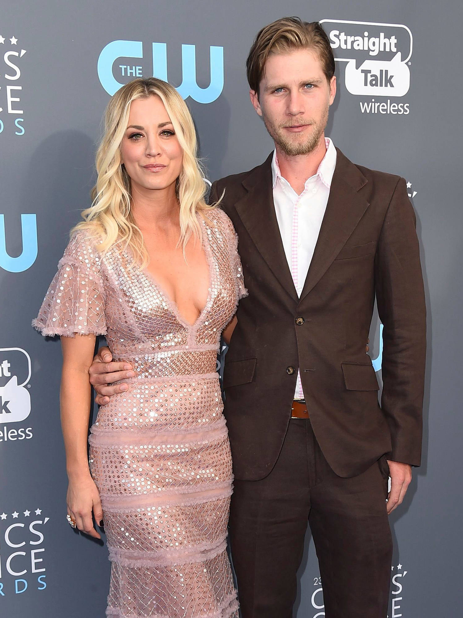Kaley Cuoco 桌布 壁紙 — 一對魅力情侶在深色背景帶有標誌的紅地毯活動上擺姿勢。